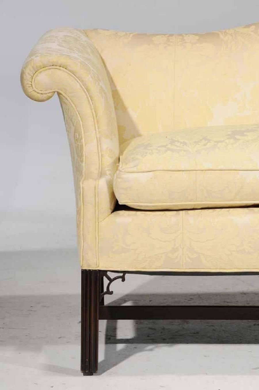 Chippendale style, mahogany and yellow damask upholstered camelback sofa, 20th century. Arched back and rolled arms, set with a down seat cushion.