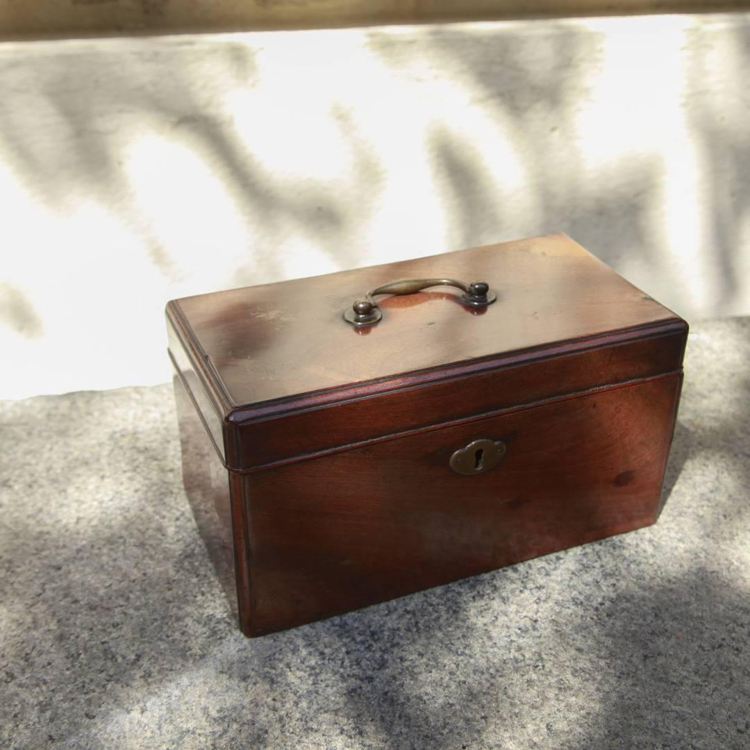English 18th century mahogany document box with thumb carved edges, a brass escutcheon, and a brass bail handle on the lid. The interior is open but shows signs of two removed partitions, leading one to believe that it started life as a tea caddy