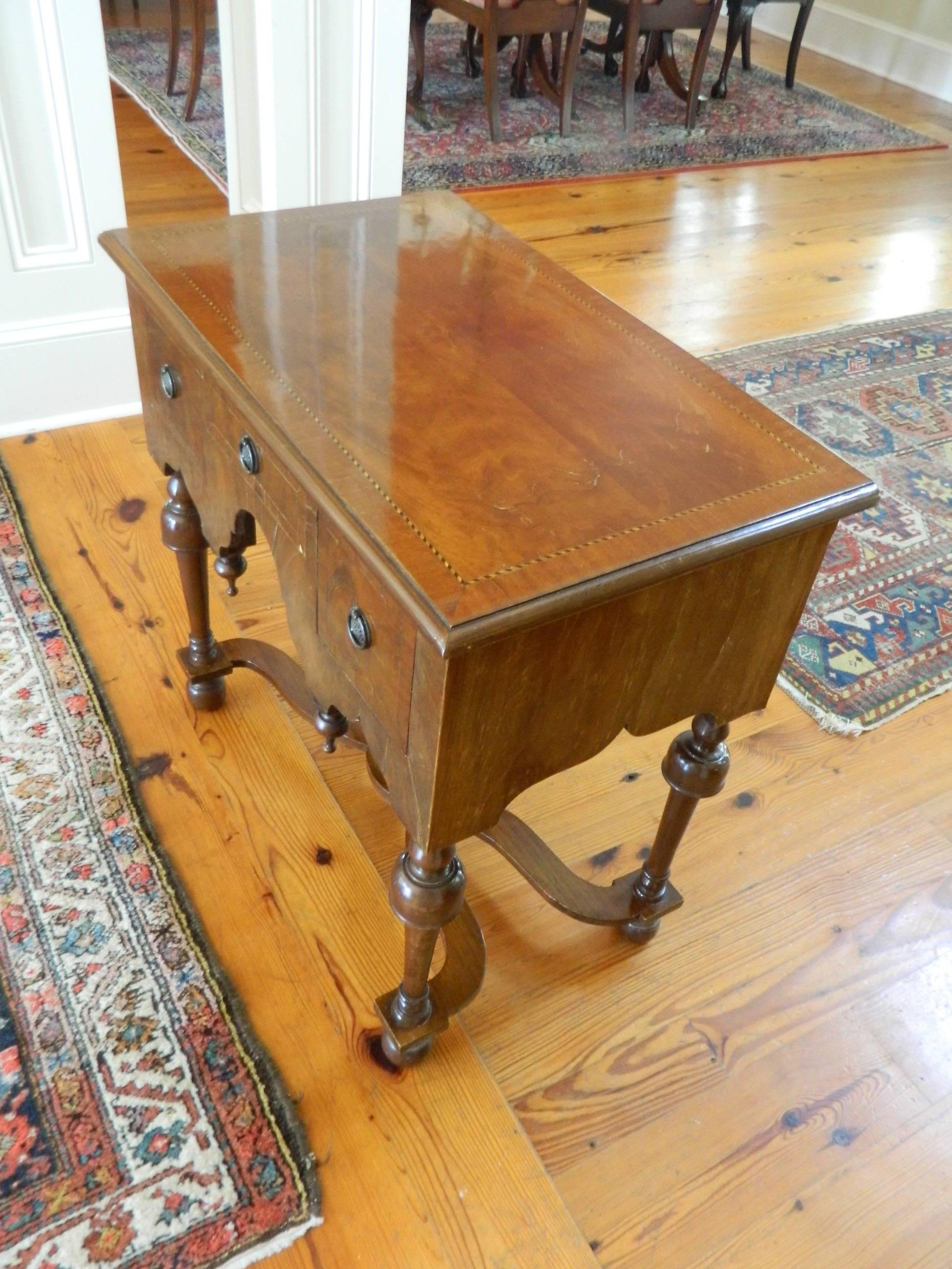 George II Mahogany three-drawer lowboy or dressing table, 19th century. Inverted finials at the skirt of its center knee hole arch. Raised in cup and ball baluster legs connected by a stretcher and bun feet.