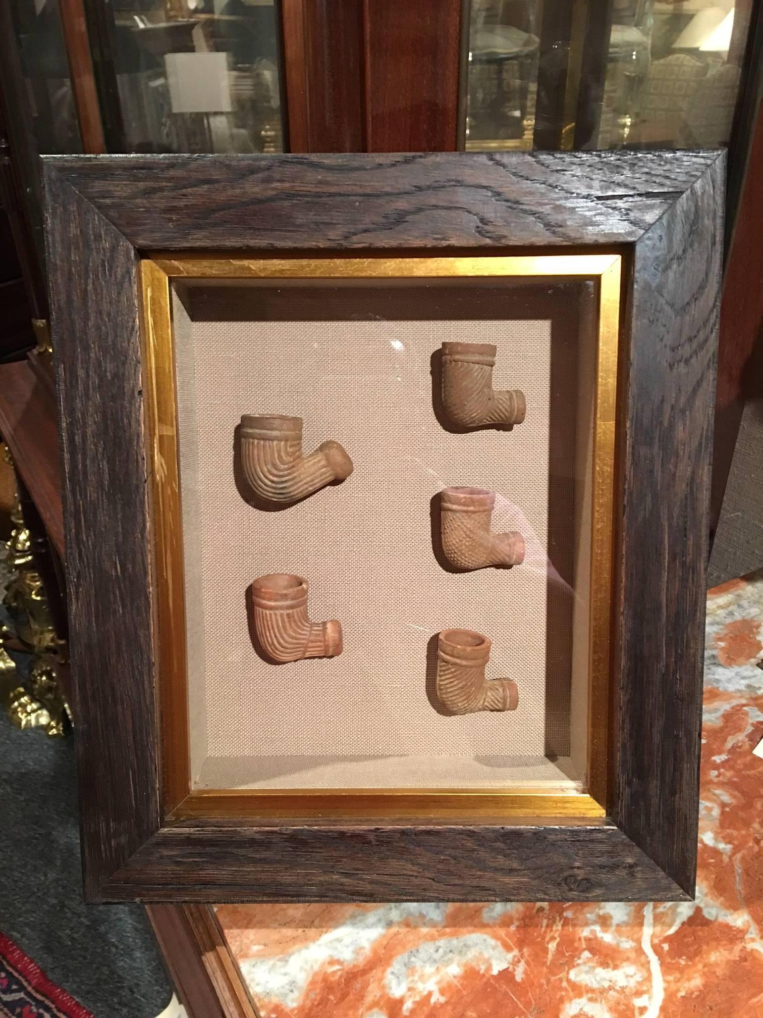 Set of five terracotta pipes framed in a shadow box, 19th century. Linen matting. Native American.