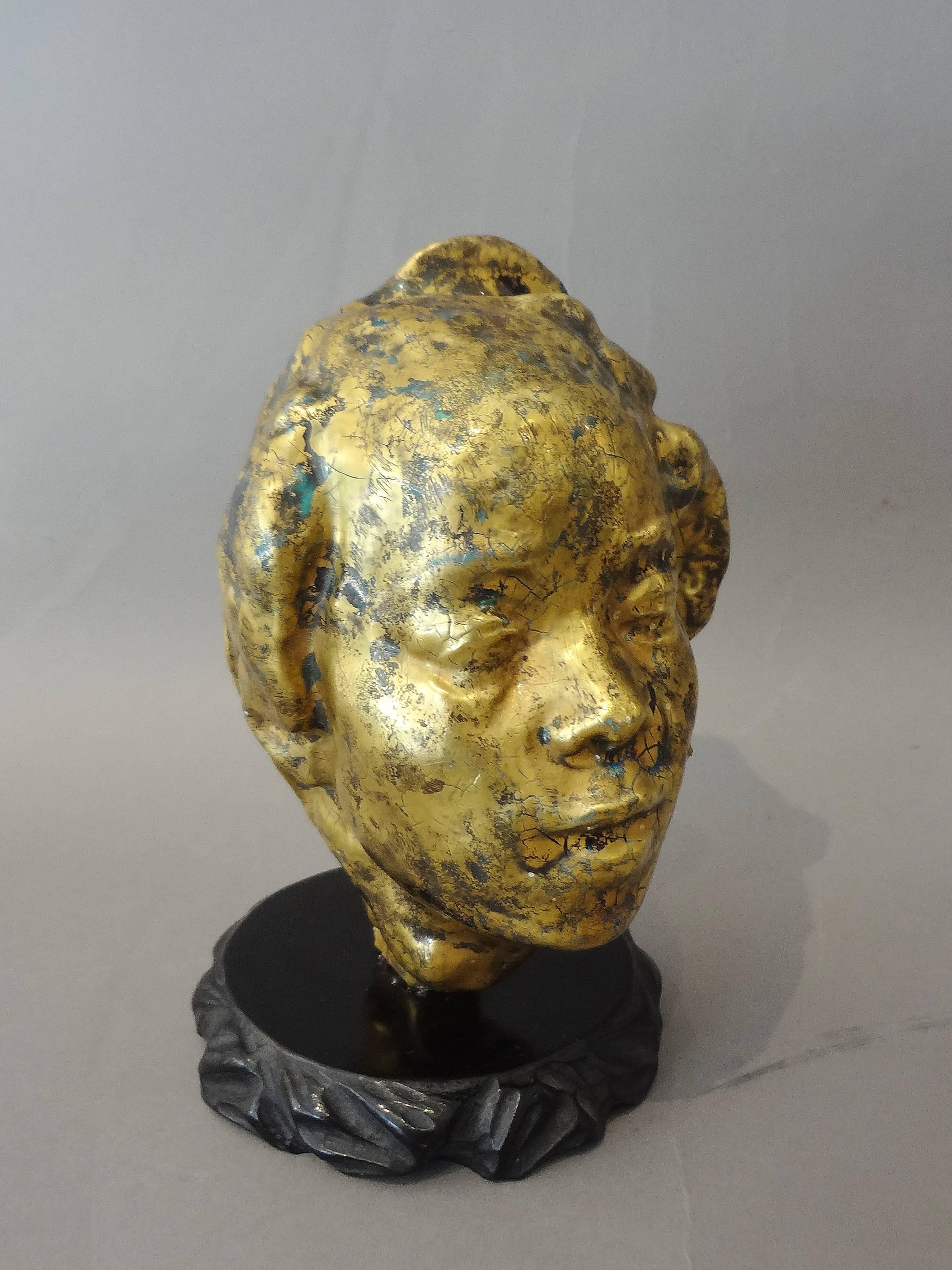 Exceptional ceramic woman’s head, 1930s, by Jean Mayodon (1893-1967)
called Hanako after Auguste Rodin.
Gilt and dark green enamelled ceramic. Unique piece.
Black circular carved wood base.
Measures: Ceramic height 14.5 cm.
 
Moving homage to