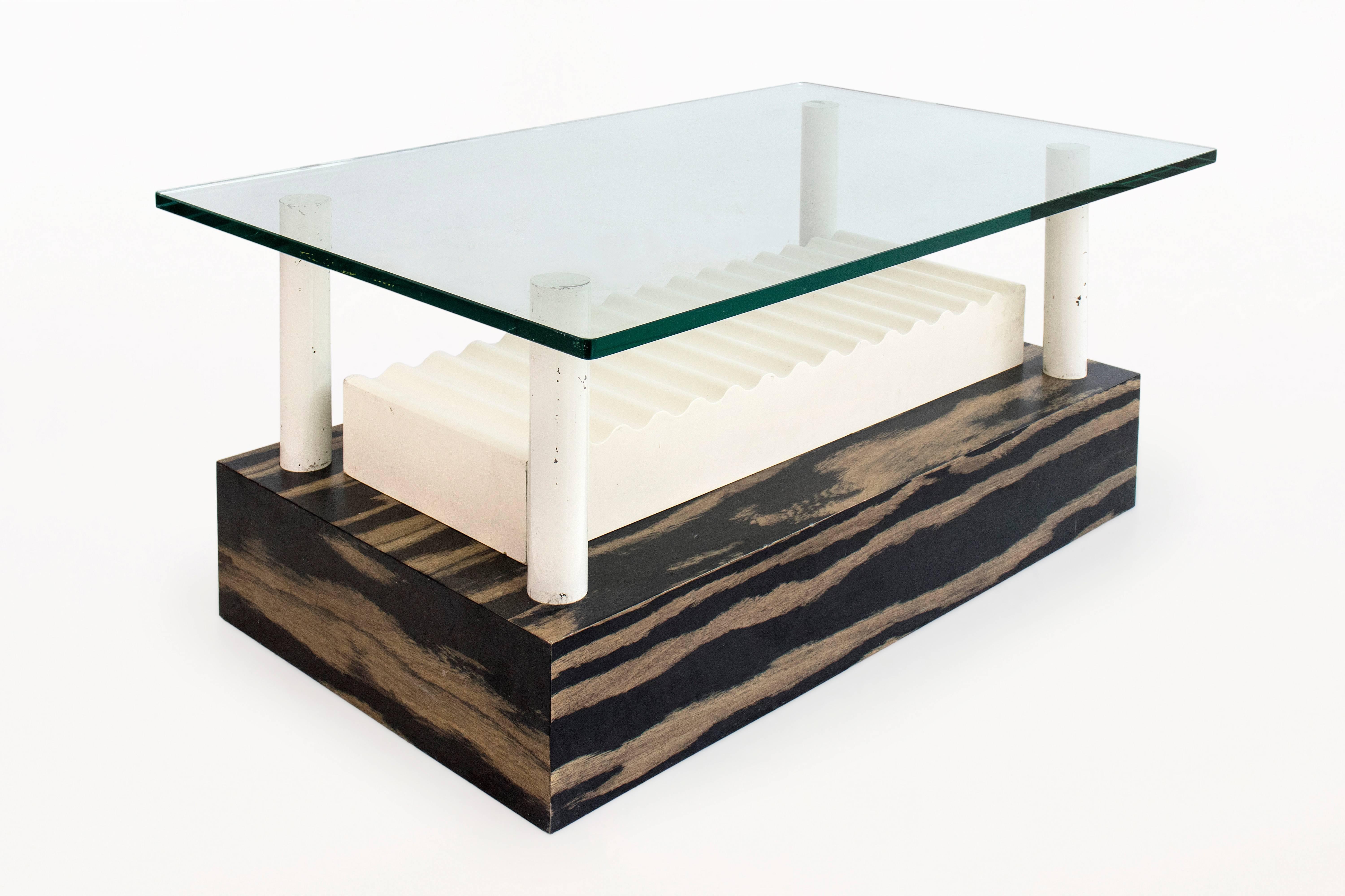 Memphis Milano coffee table by Ettore Sottsass for Alessi
unique, one-of-a-kind
Designed by Sottsass for Alessi
glass top suspended by 4 lacquered metal columns positioned in a laminated wooden base with figurative wave center piece
Provenance:
