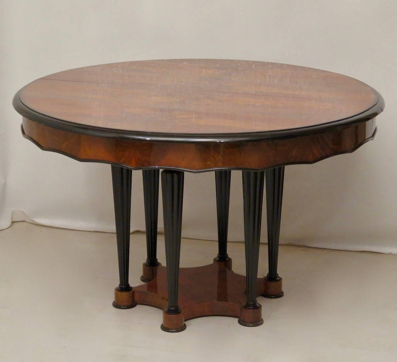 An important Biedermeier table, with a big round top and a very particular leg. The tabletop is veneered with a beautiful walnut with parts forming linear segments. The central leg is formed by many small black lacquered legs. The open table has two
