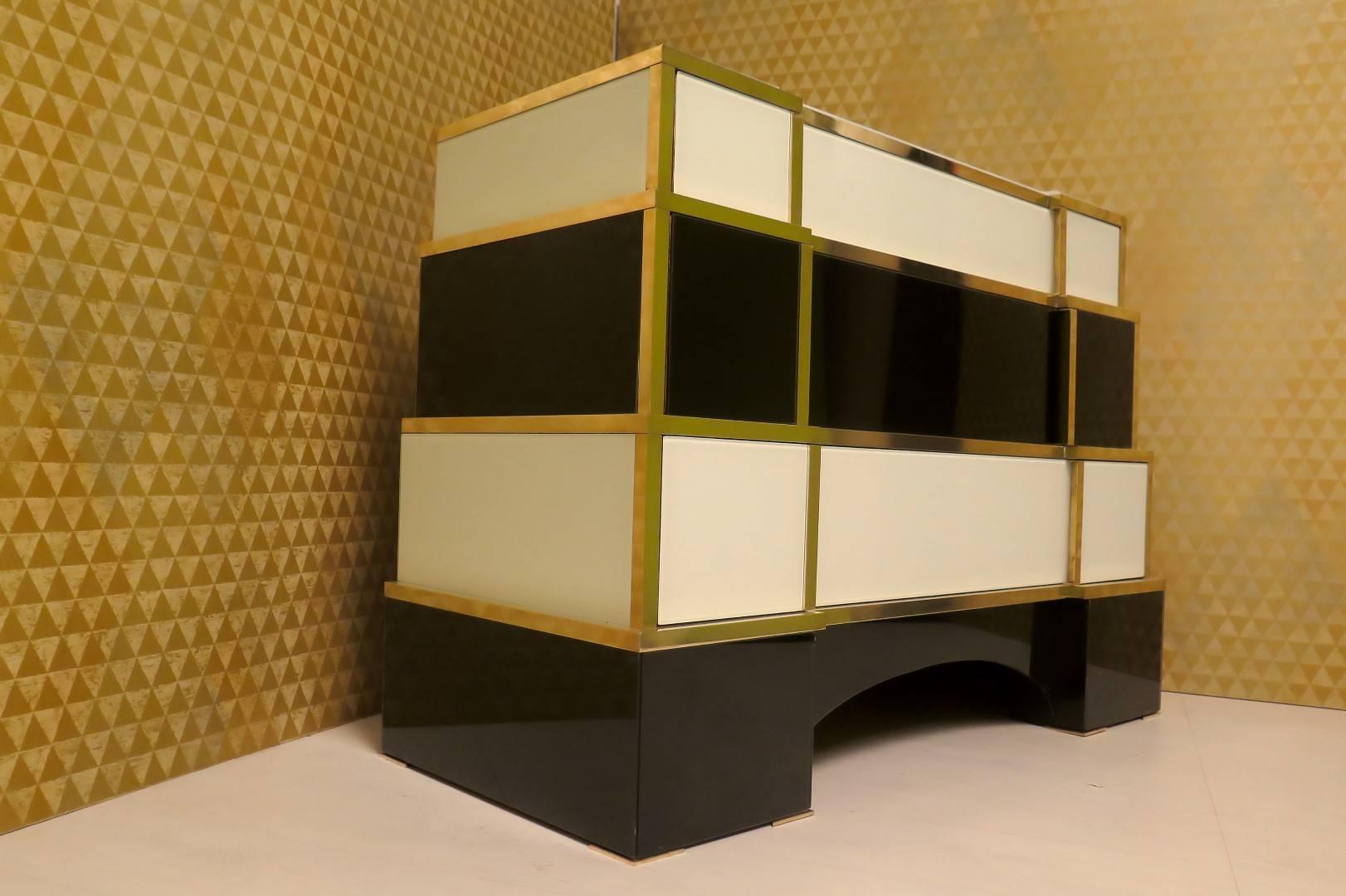 Chest of drawers with wooden body, edges finished in brass and coated in colored glass in black and white. Very special design with the body that tapers, as a pyramid, from the bottom upwards, on the edge you can see the brass finish. With three