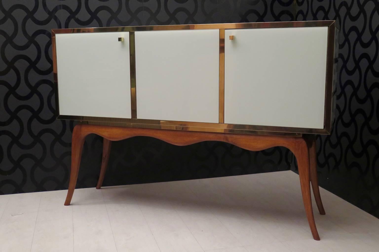 Lovely Venetian sideboard 1950s, body in white lacquered glass and brass edges, the leg is in cheerywood. Its particular shape, a big glass box and brass over a beautiful leg movement. Three doors, two with shelves and one with internal drawers.