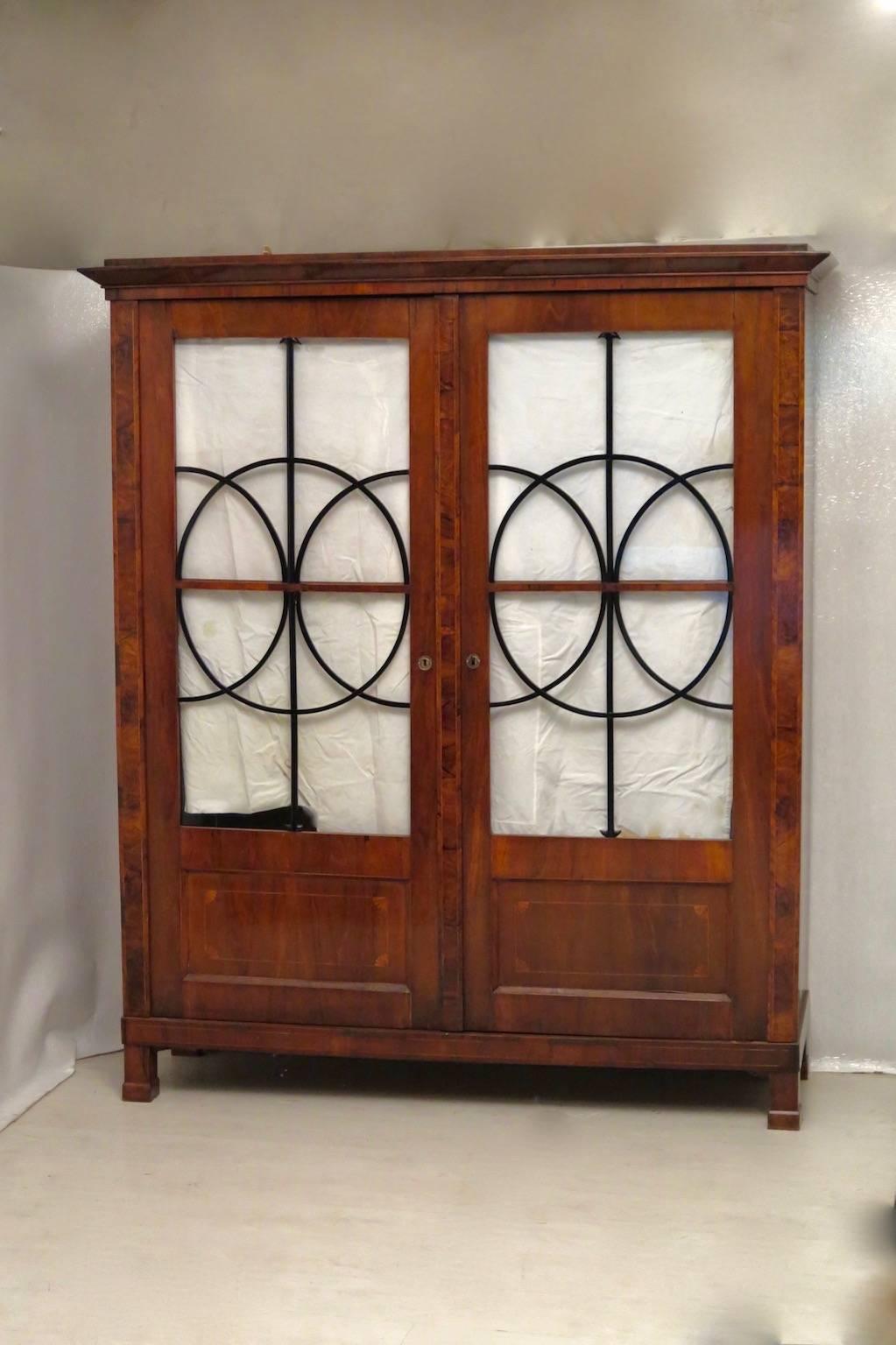 Austrian Biedermeier bookcase. All veneered in walnut, with lighter wood for the inlays. Squared, with two large front doors. These are formed by a large frame, with a wooden screen at the bottom and with a glass at the top. The part with the glass,