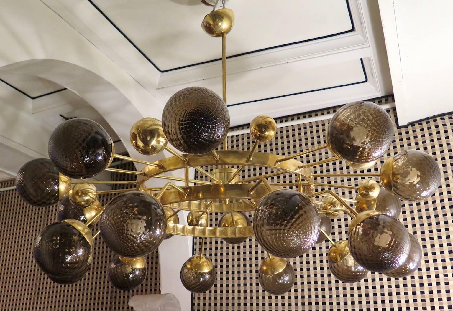 Particular circular sputnik, with brass structure and Murano glass spheres. It looks like a system of planets that gravitate circularly.

Chandelier with all brass structure, and amber colored glass spheres. A double brass structure of round shape,