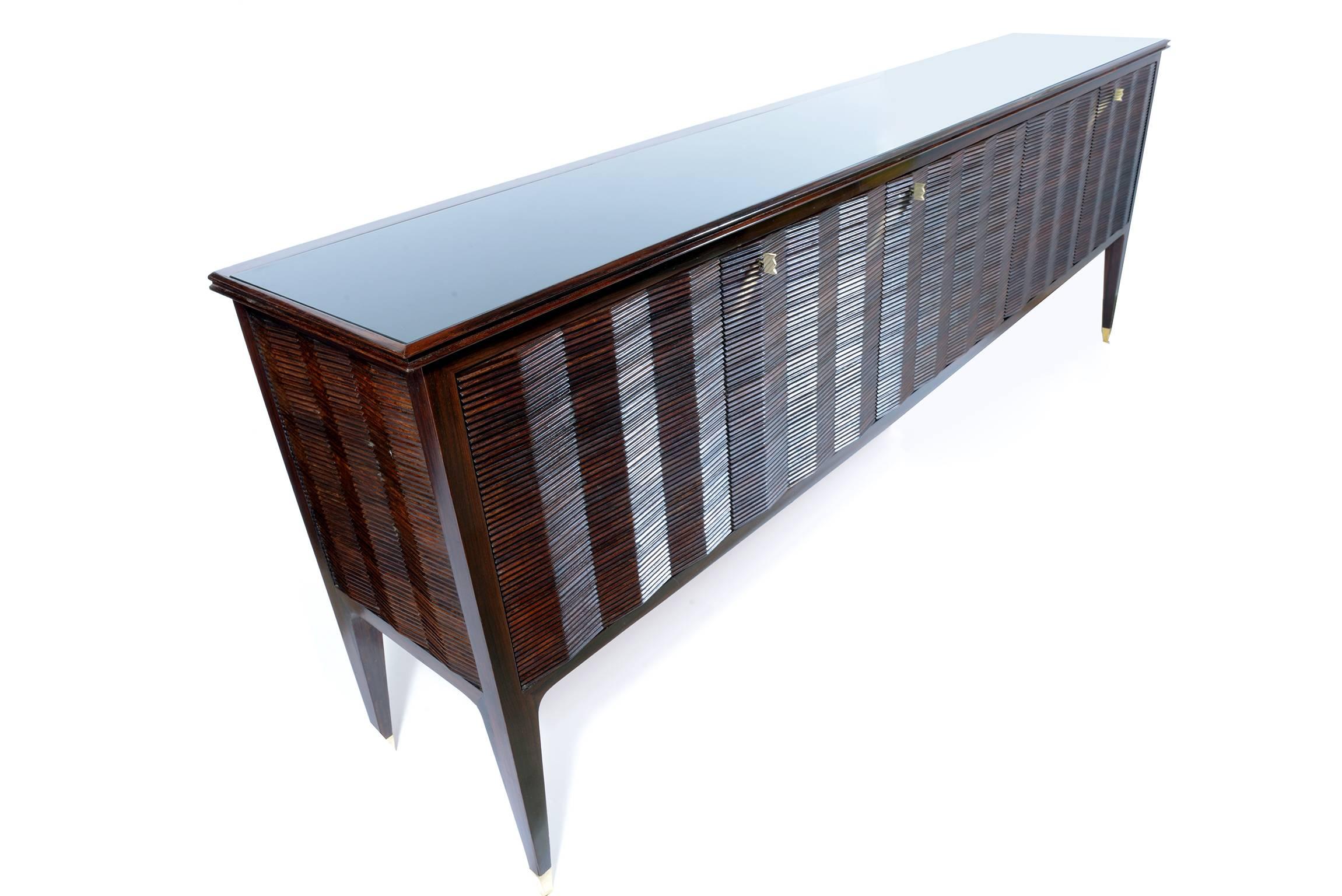 Elegant and unusual sideboard solid exotic precious grooved wood to create a repetition of corner, cuts brass beautiful shaped feet and keys.
Encased black glass top.
Interiors on cheerywood with shelves.
Signed.