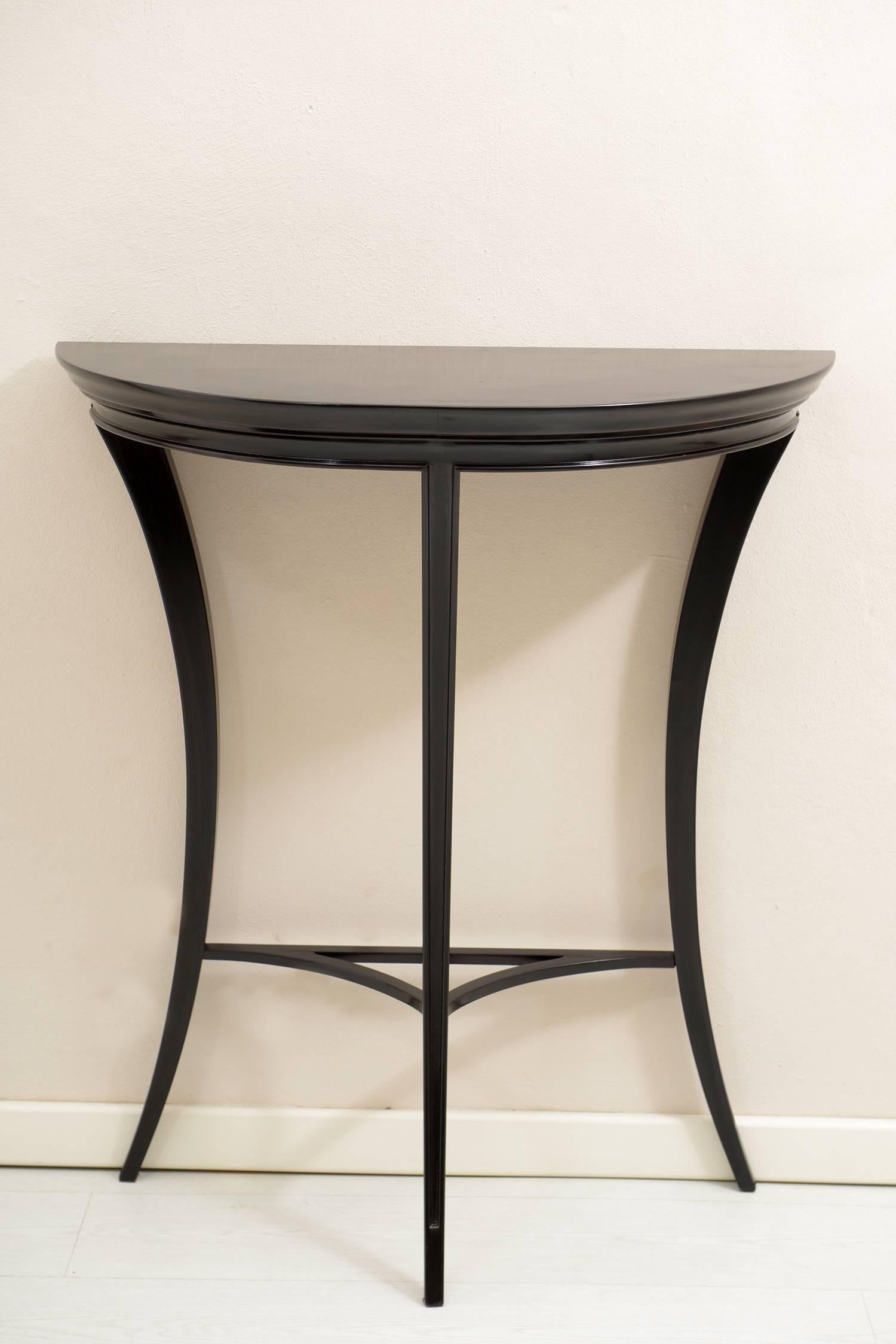 Solid wood black laquered console three slender and curved legs sustain a demilune top.
 