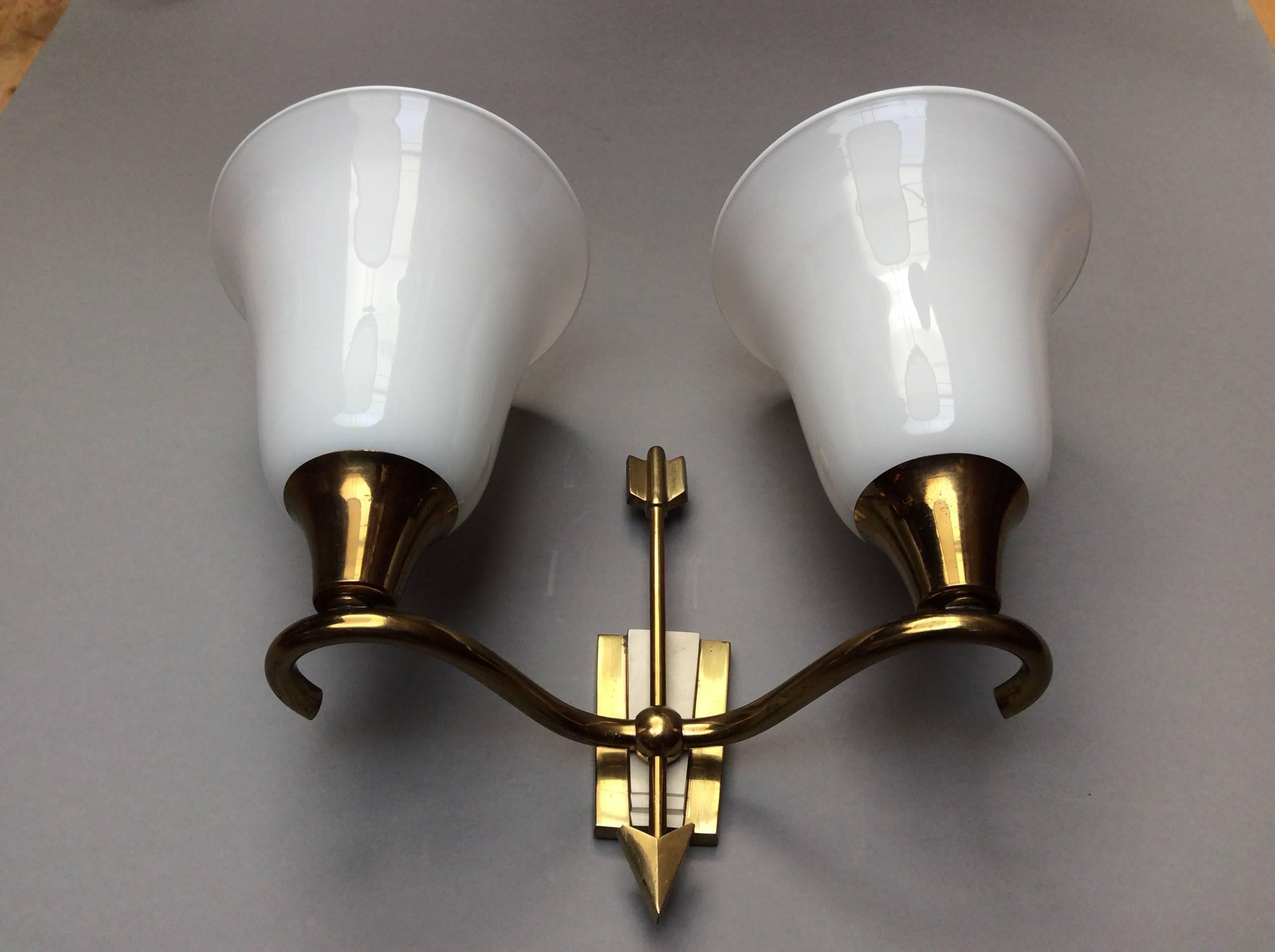 Brass cast structures with two arms and stylized arrows, partially white laquered. Two beautiful Murano blown glass white bolws ich sconce.
The price is for Two sconces.