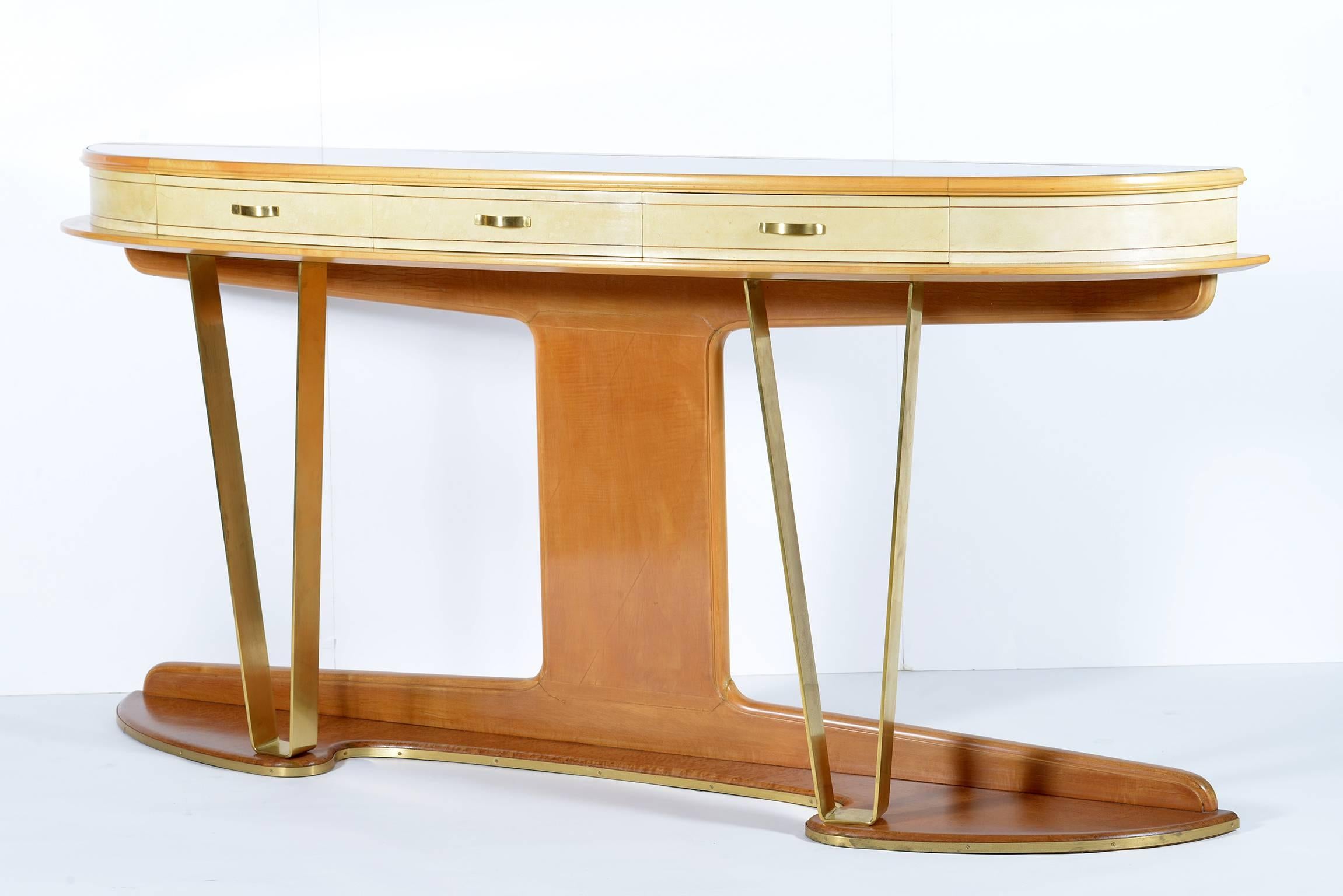 Solid maple wood structure with three drawers covered in parchment  inlaid with walnut   .
Beautiful demi lune shaped top with encased gold glass ,  bird eyes maples wood base edged by a brass rod that follows the sinuous shape of the edge.
Two