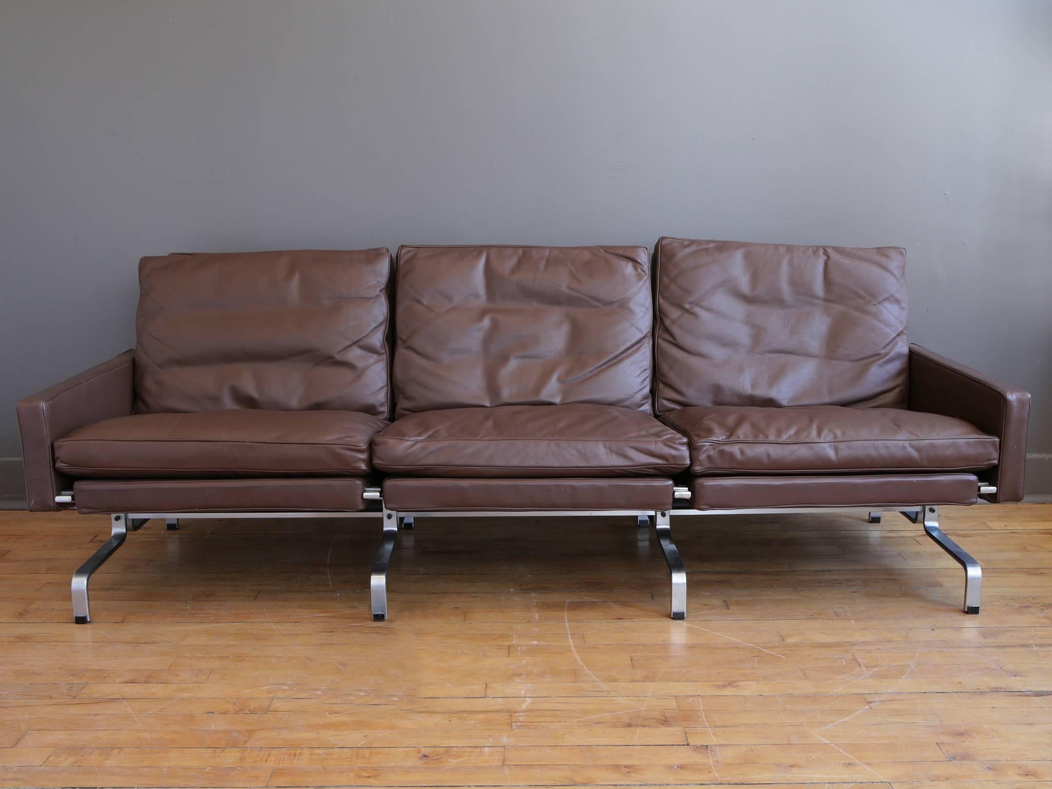 A three-seater sofa designed by Poul Kjaerholm for E. Kold Christensen, circa 1960. Upholstered in chocolate brown Spinneybeck leather. EKC stamped mark to underside of matte chrome-plated steel frame. 