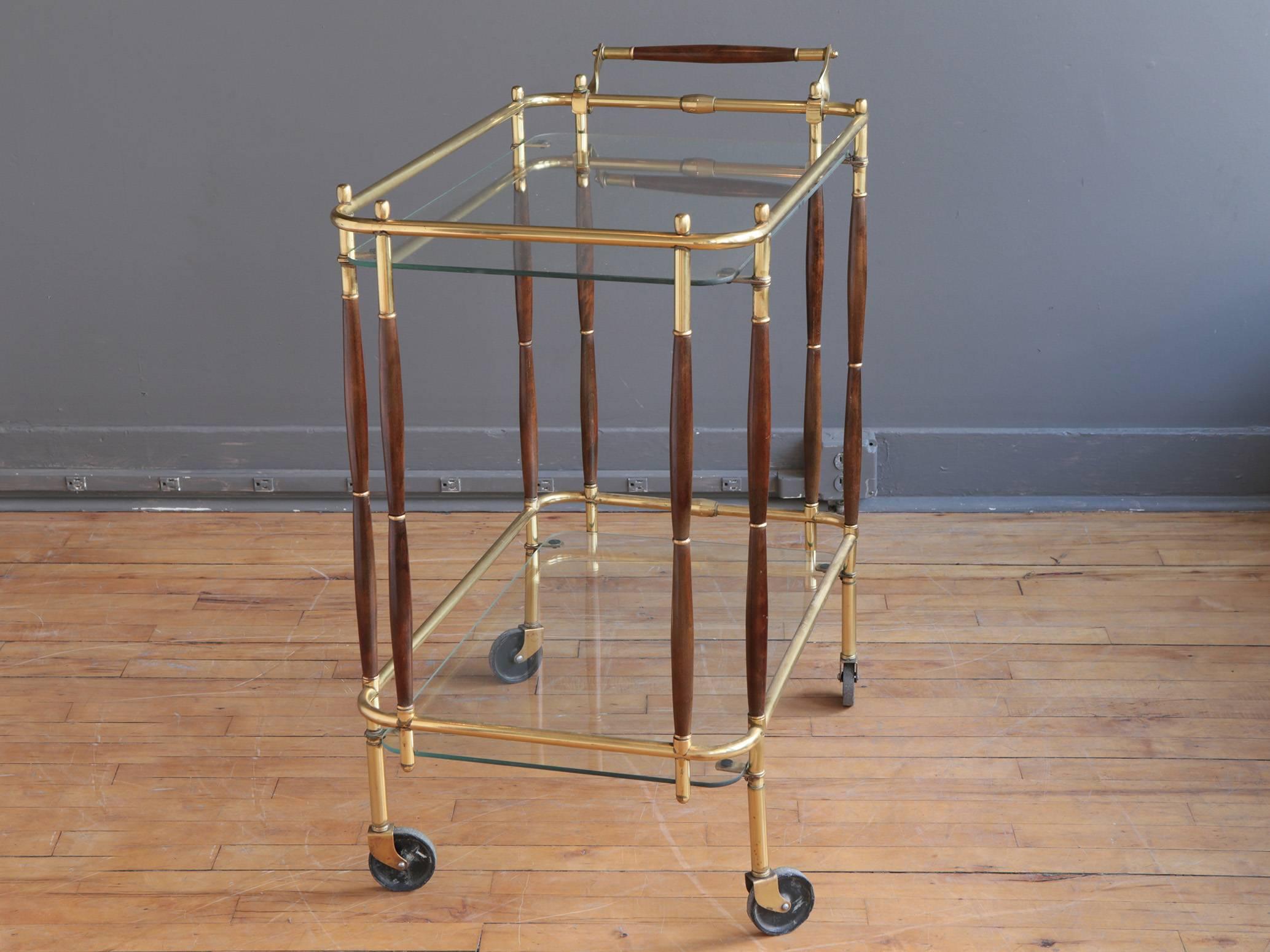 An Italian bar cart in the style of Cesare Lacca, circa 1950s or 1960s. Featuring a tubular brass frame with turned walnut supports and handle. Two removable glass shelves provide storage and serving areas. 

Simultaneously chic and functional. A