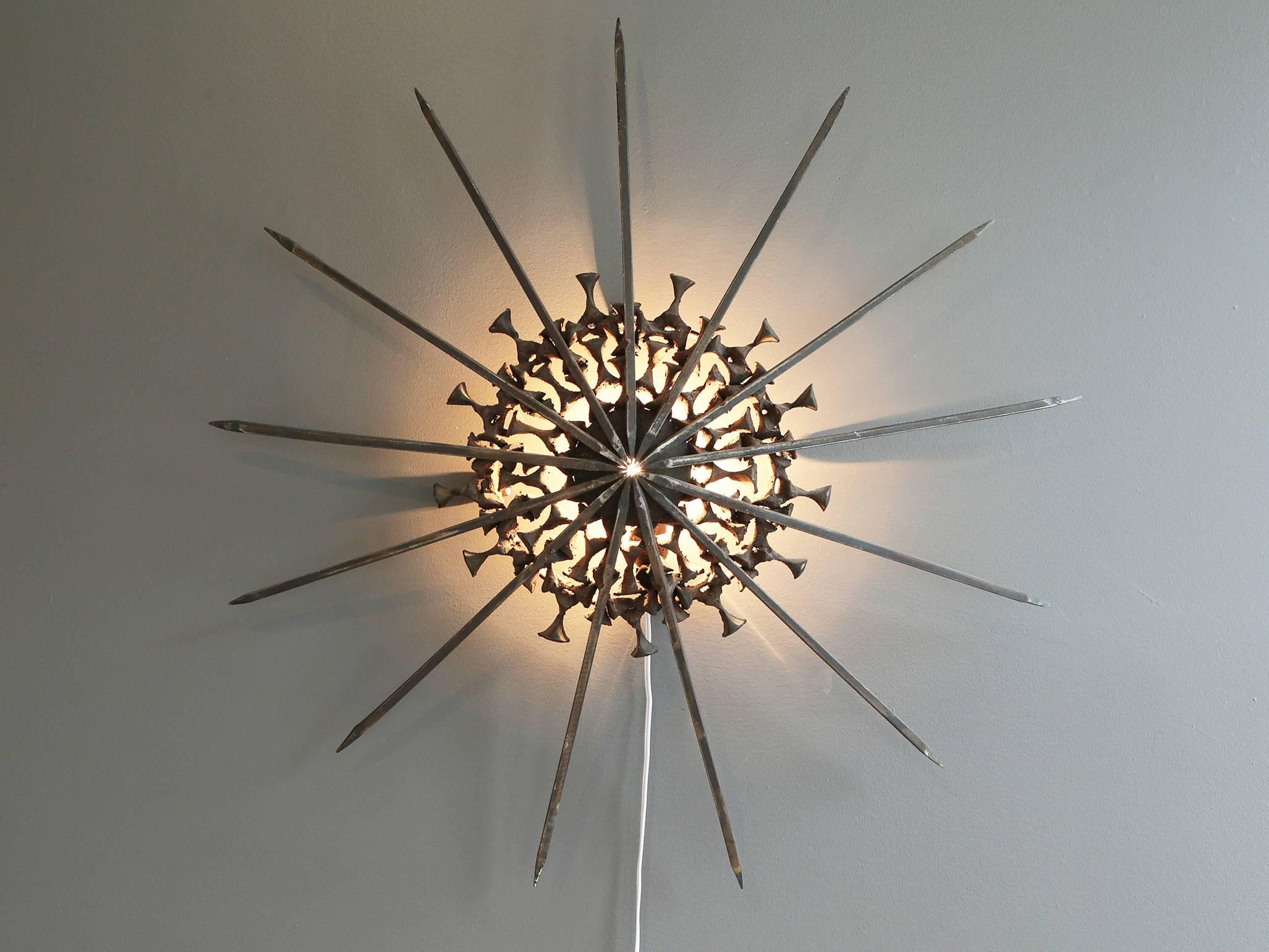 A Brutalist handcrafted iron wall sconce attributed to Chilean sculptor Sergio Castillo, circa 1970s. Consisting of iron rods arranged in a starburst pattern backed by concentric circles of individually cast iron pieces. 

Creates a warm,
