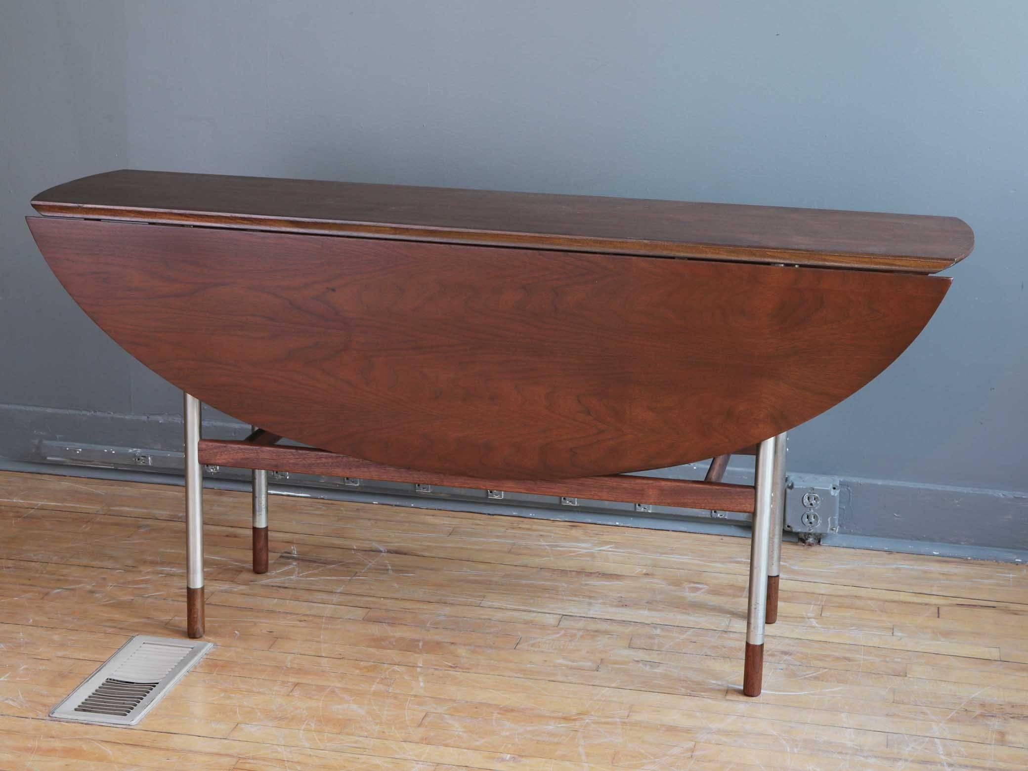 An oval drop-leaf dining table attributed to Danish designer Arne Vodder for Sibast, circa 1960s. Featuring a bevelled maple top with dark brown finish, matching apron and stretchers, and brushed steel legs with handsome wood caps. Recently