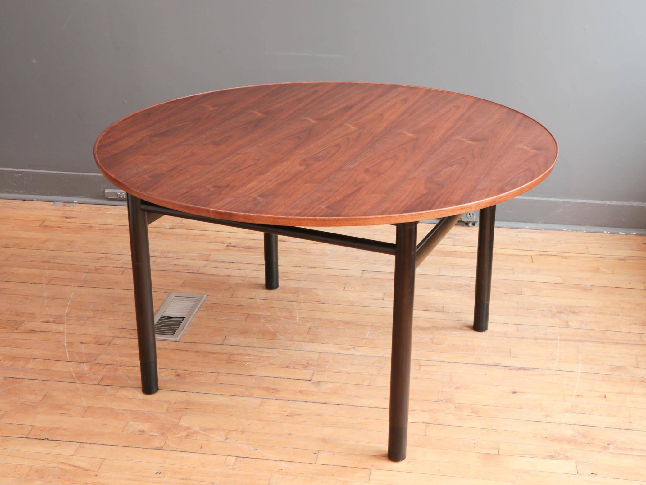 A very handsome dining table designed by Edward Wormley for Dunbar, circa 1950s. Featuring a round walnut top with raised lip supported by a black lacquered mahogany base. Each leg finished with a subtle leather cuff. One removable leaf allows table
