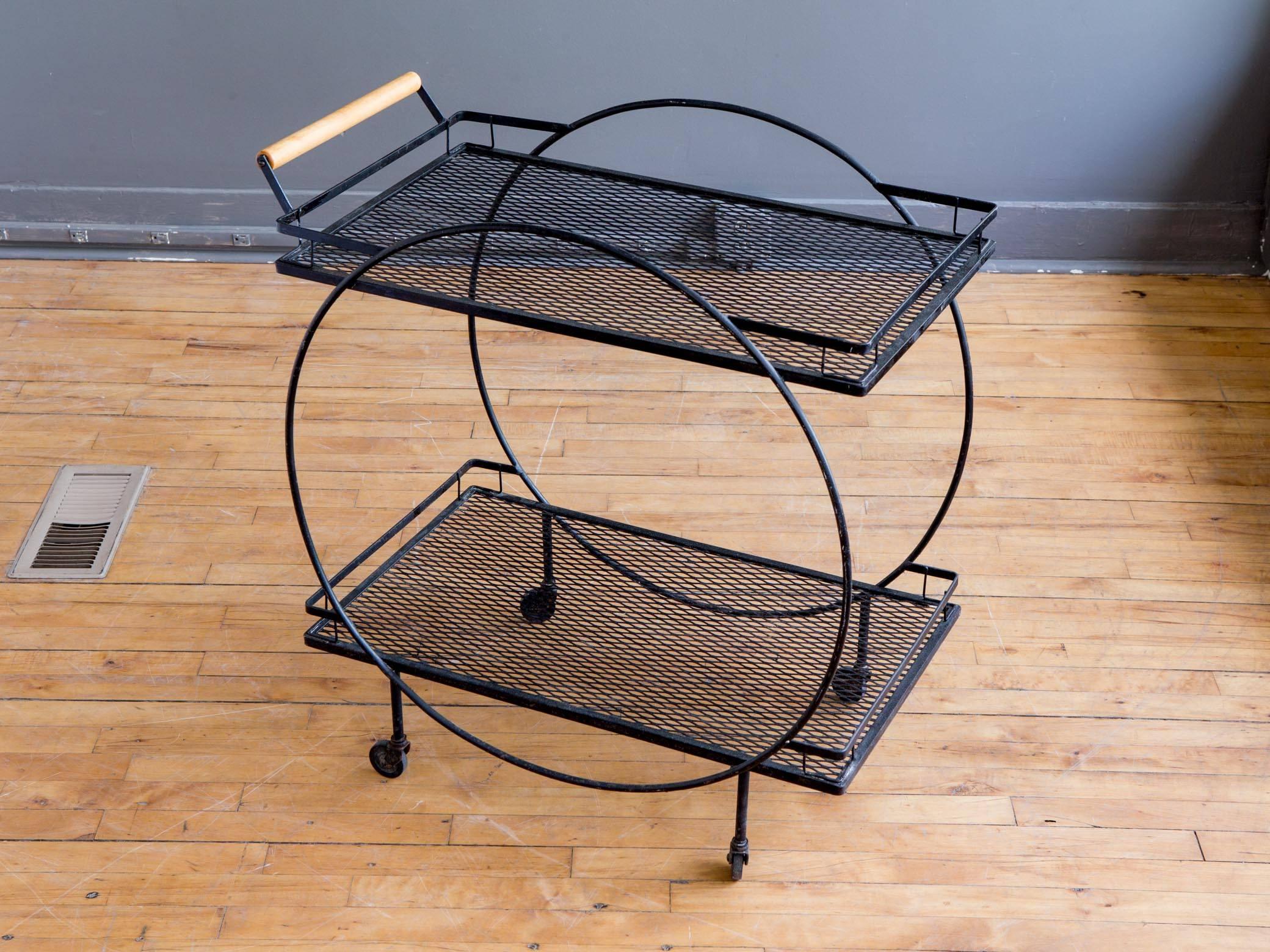 An iron bar cart or drinks trolley by American Industrial designer Freda Diamond, circa 1950s. Featuring a circular black frame with two metal mesh shelves all supported by four rubber casters. Round handle bar is fashioned from maple. A graphic and