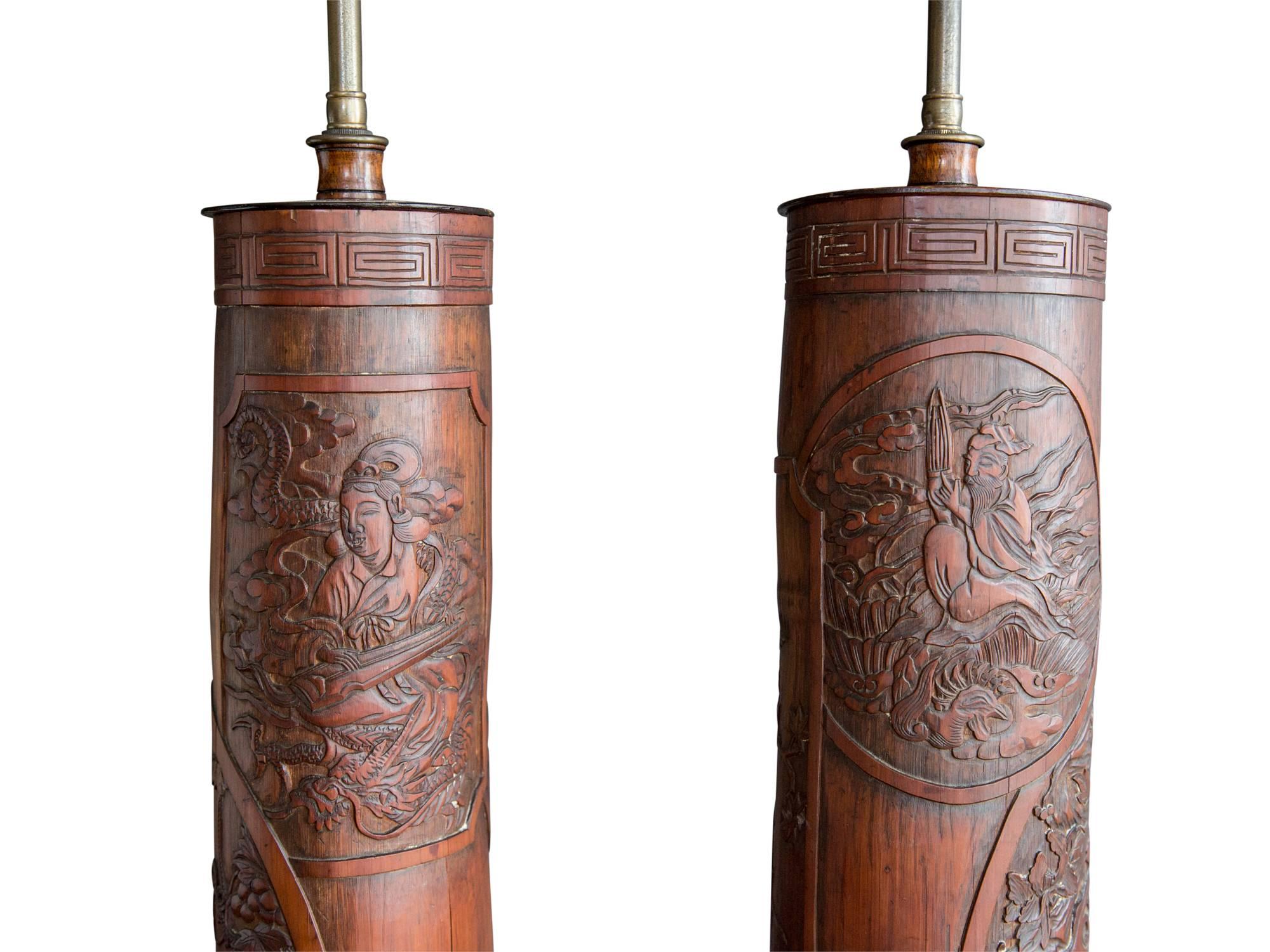 A decorative pair of antique Chinese Export table lamps. Most likely late 19th or early 20th century. Featuring carved bamboo shafts with classic motifs such as a scholar and musician, dragons, and birds. Mounted on hexagonal black lacquer bases and