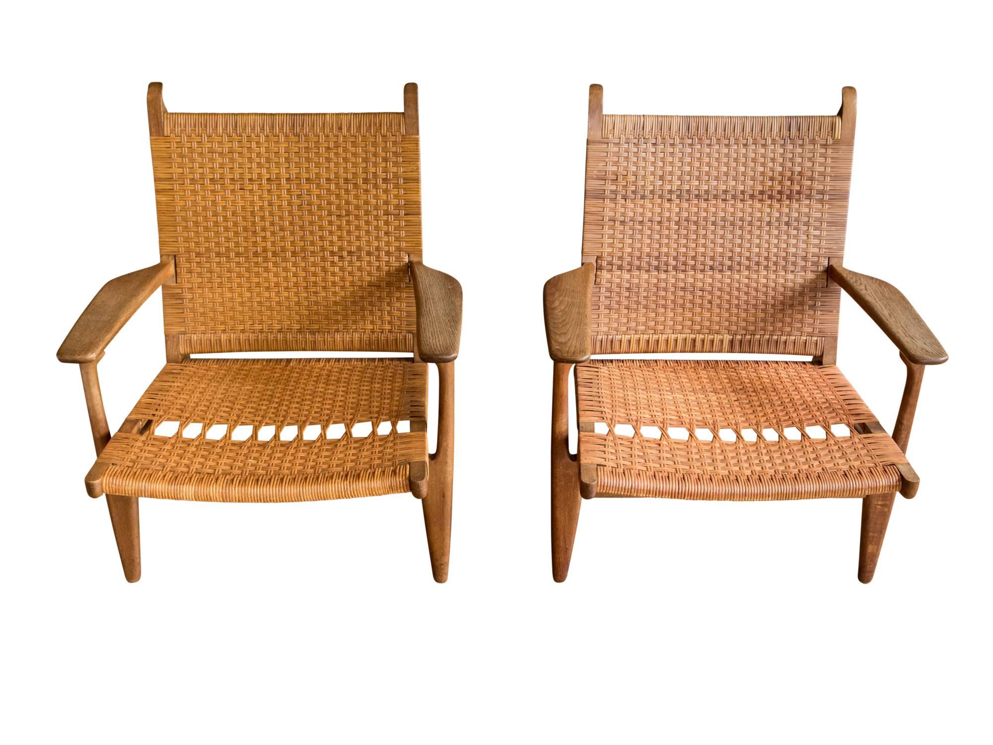 A handsome set of model CH-27 lounge chairs by Hans J. Wegner for Carl Hansen & Son. Designed in 1949, this set dates to the 1950s. Featuring solid oak frames with woven cane seats and backs. Paddle arms and elegantly splayed back legs add to