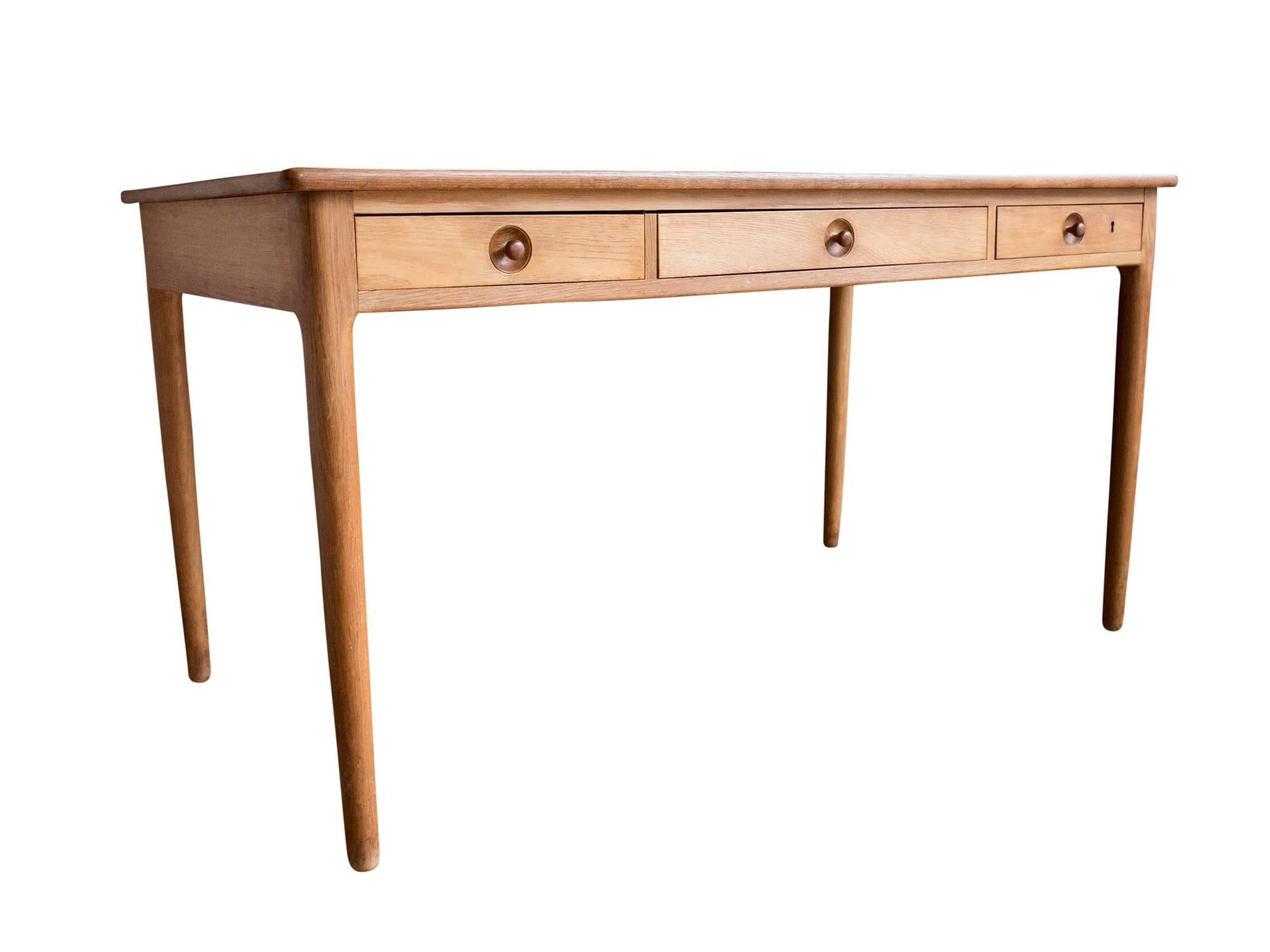A model AT 305 writing desk designed by Hans J. Wegner for Andreas Tuck, circa 1950s or 1960s. Featuring a large rectangular oak top supported by slightly tapered cylindrical oak legs. Three storage drawers finished with recessed turned knobs. Built