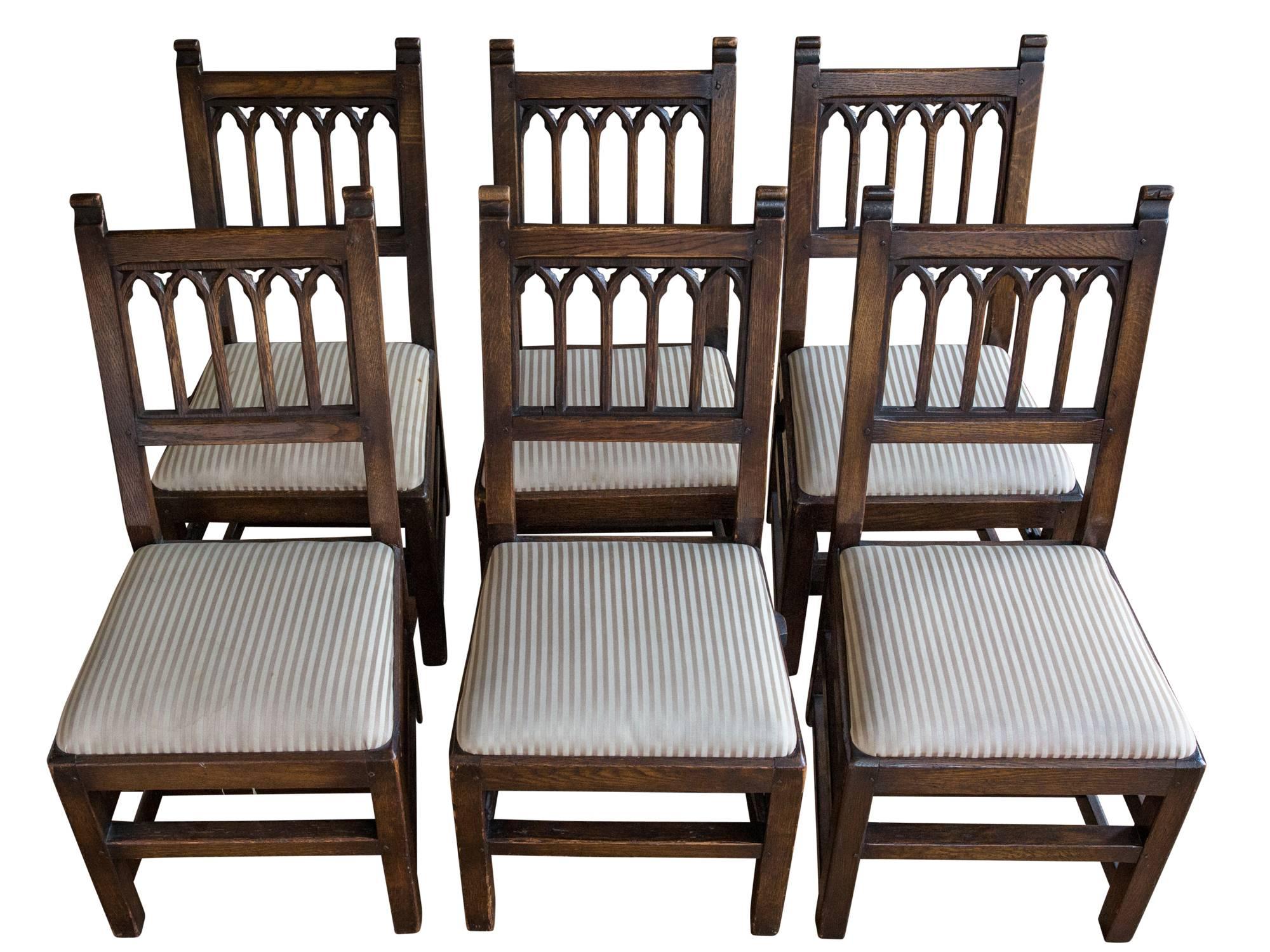 A set of six pew chairs from New York City's Riverside Church, circa 1930s. Consisting of solid carved oak frames with Gothic arched splat and upholstered seats supported by square legs joined by stretchers. Chairs also feature integrated book rack