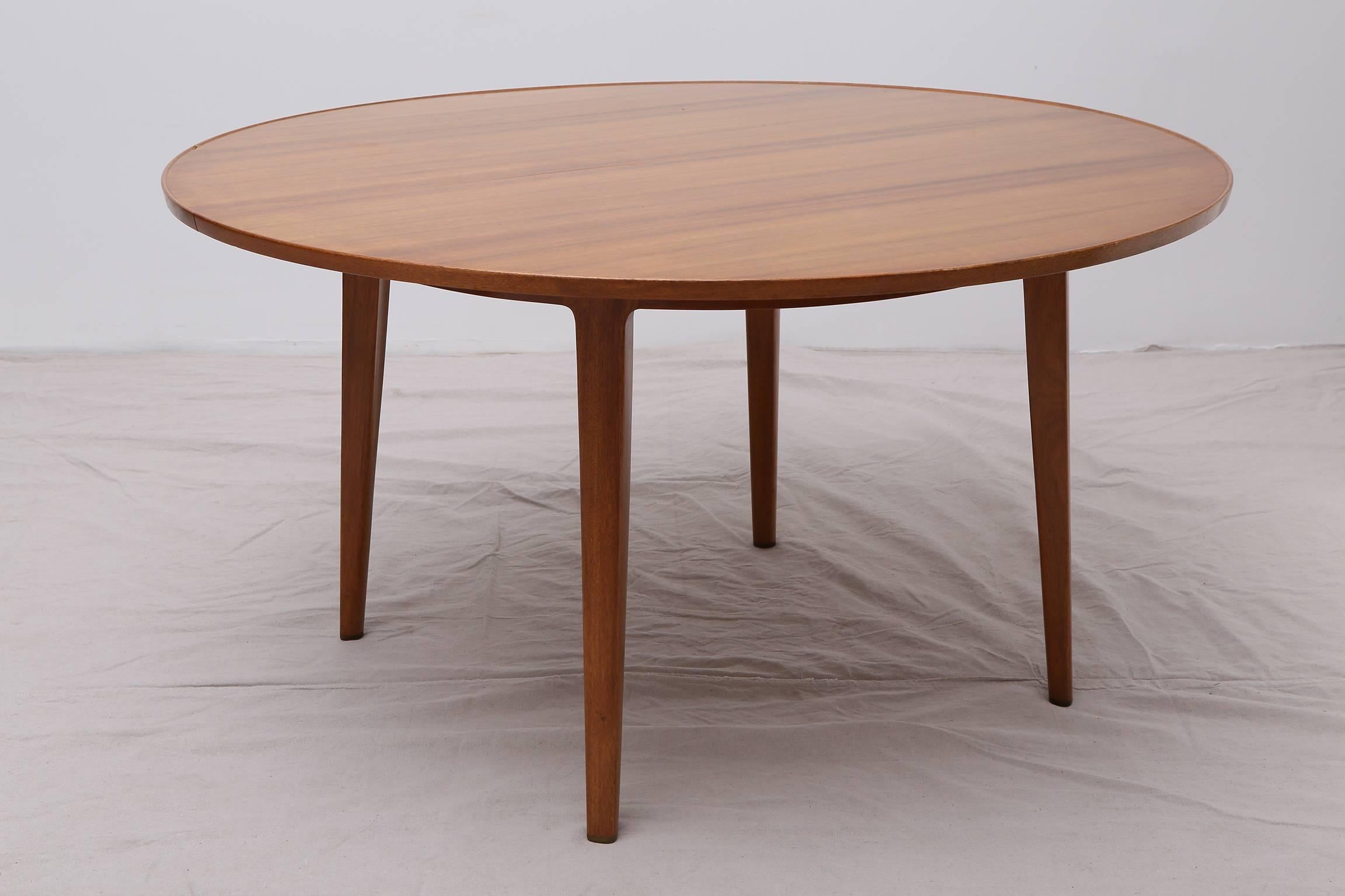 A handsome bleached mahogany dining table by Edward Wormley for Dunbar, circa 1950. Featuring a generous round top with raised lip and four sturdy, tapered legs finished with brass sabots. Two removable leaves allow table to easily accommodate eight