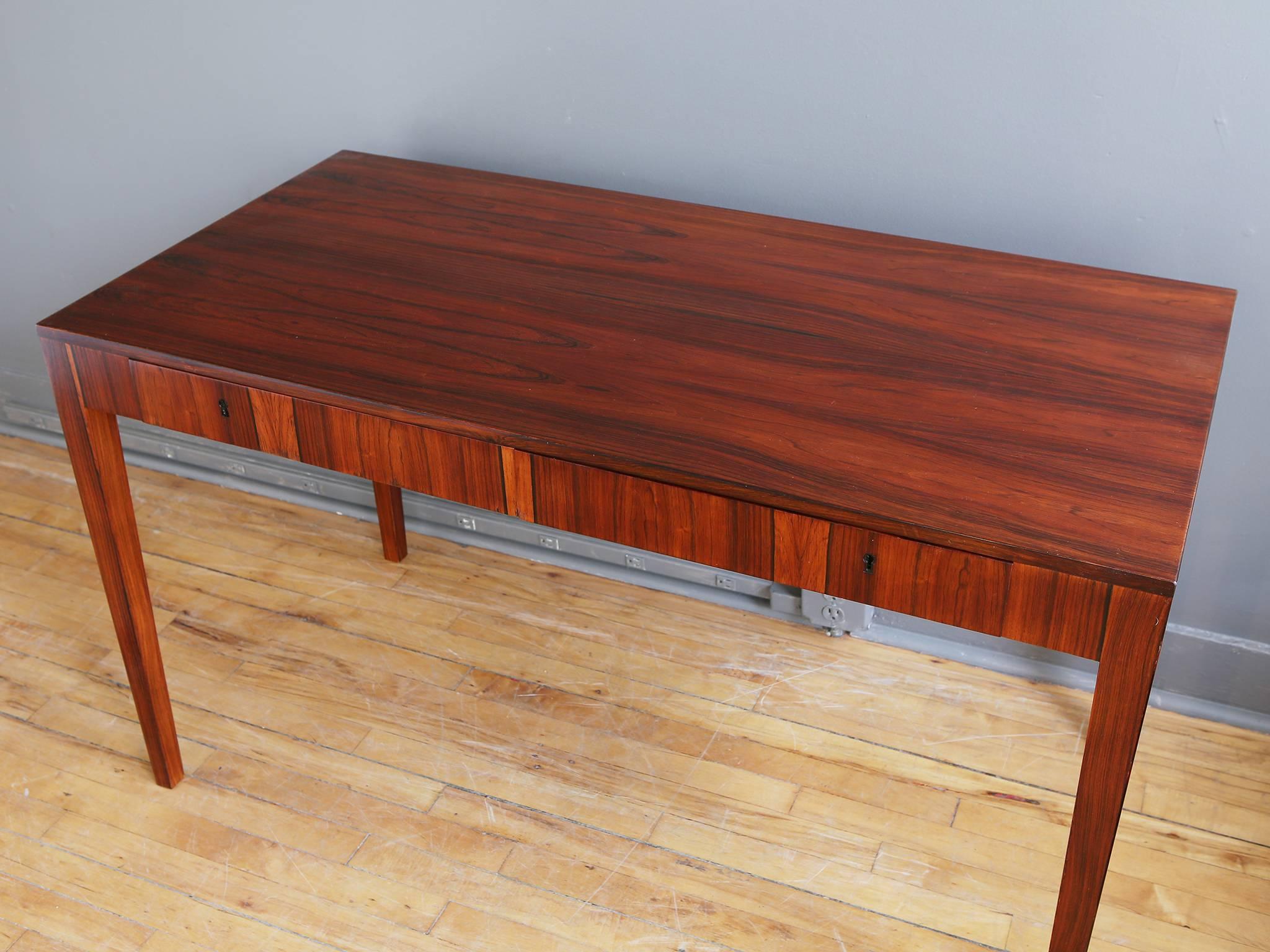 A smart Danish rosewood writing desk or library table by Riis Antonsen, circa 1950. Featuring a beautifully grained work surface with two generous drawers supported by four tapered legs. Finely made with mahogany secondary woods. 

Recently