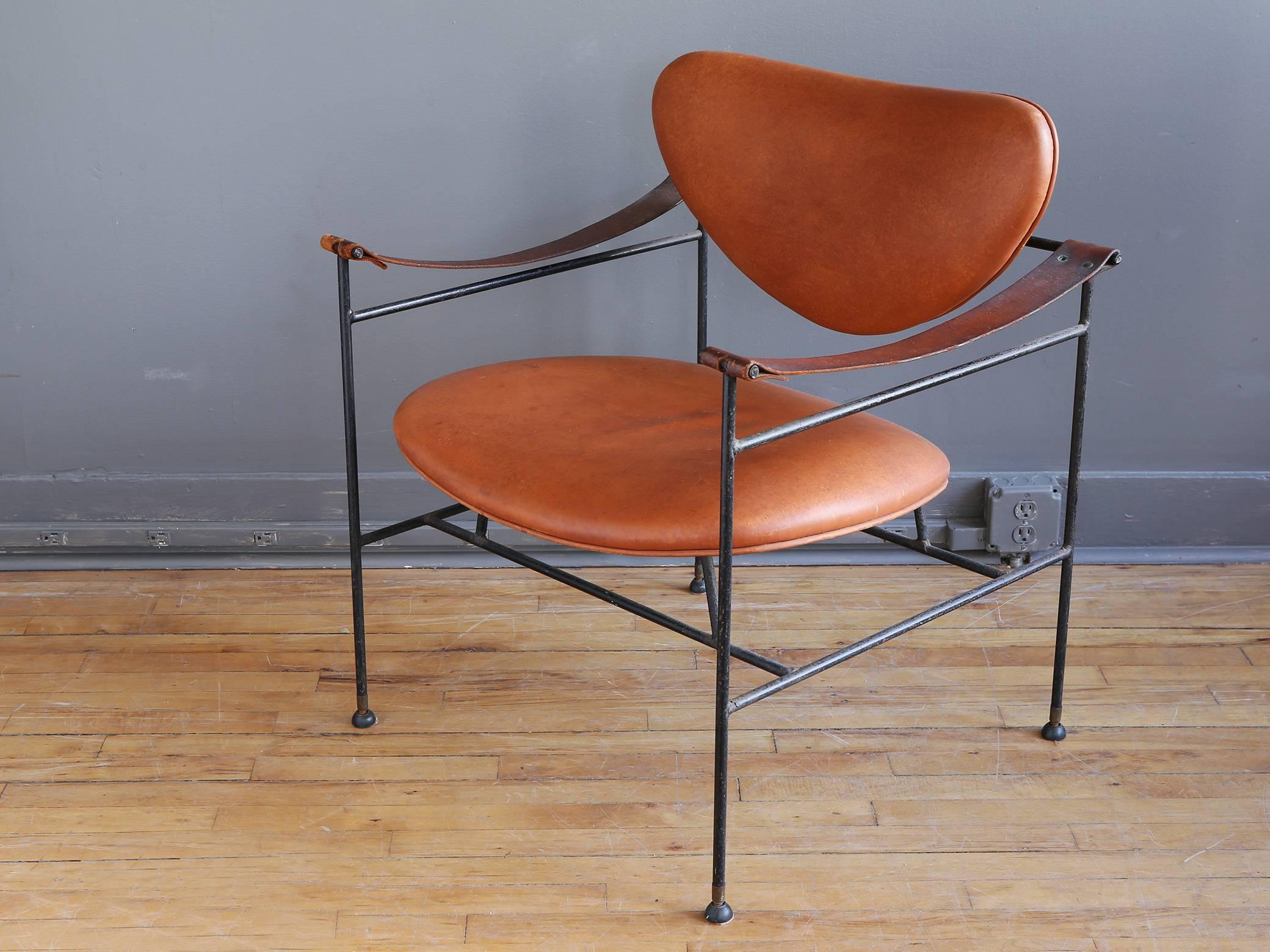 An interesting and sculptural lounge chair in the style of Danish designer Finn Juhl, circa 1950. Featuring a wrought iron frame with seat and back cushions upholstered in distressed cognac leather. Leather sling armrests show a warm patina.