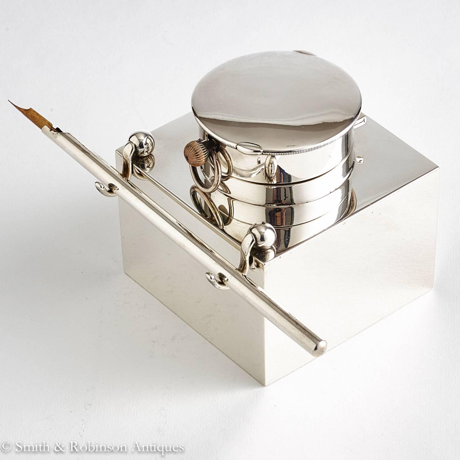 A fine quality novelty silver clock inkwell with pen and rest on front leading edge.

The interior has a cut-glass well which is held in position with two silver struts with inscribed details of the retailers, Goldsmith & Silversmith Company,