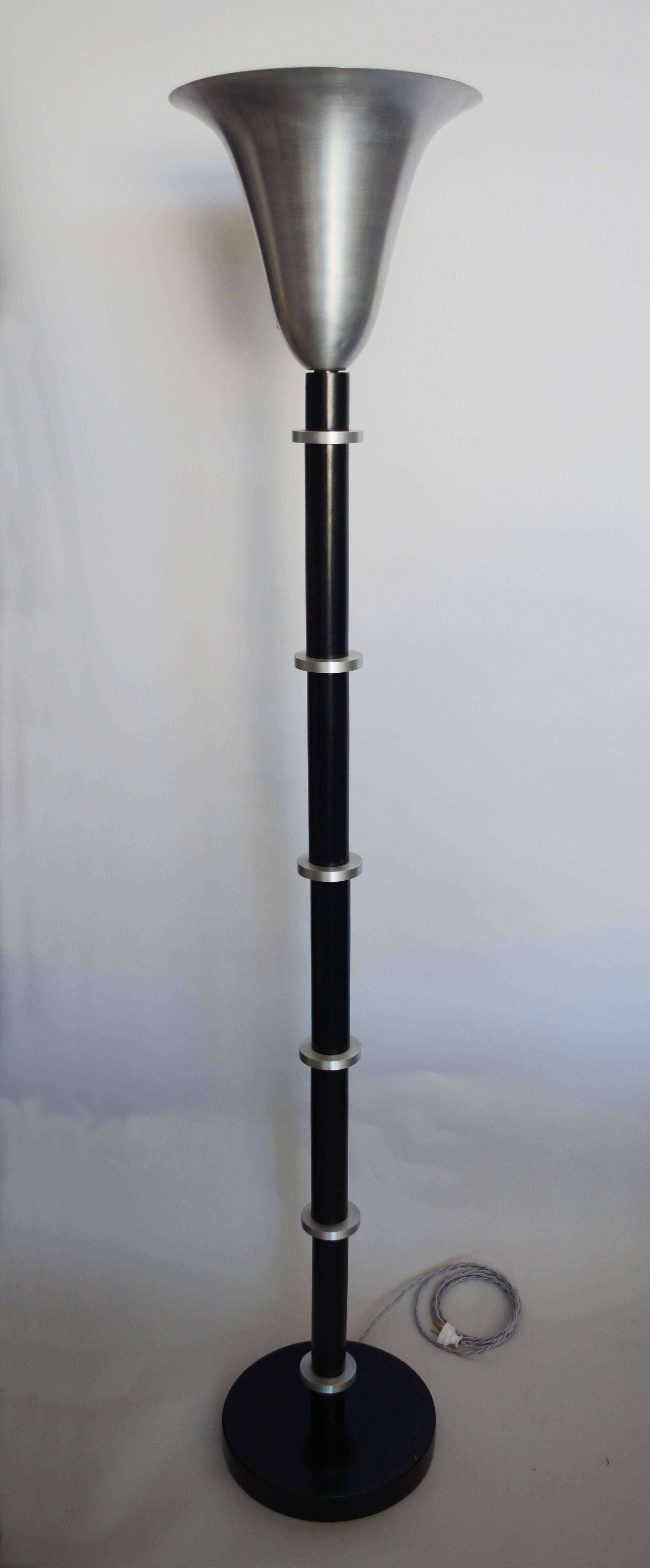 The columns of these torchieres are black lacquer with aluminum discs. The bell shaped shades are aluminum. These have been rewired and have new switches and sockets. The socket takes a mogul base bulb. An adapter can be used in the socket to enable