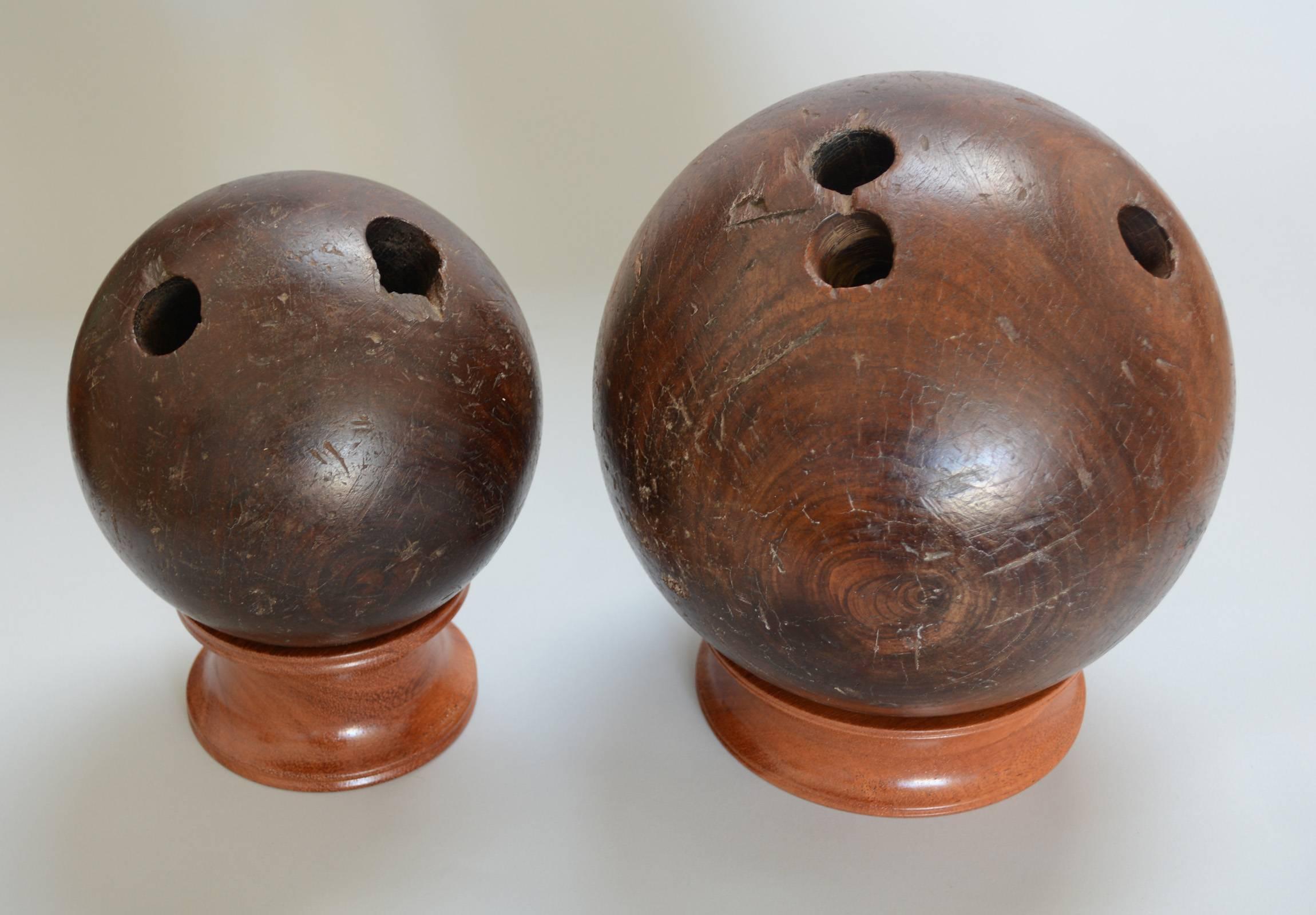 Two early 20th century bowling balls made from lignum vitae. These are on mahogany stands. The smaller ball is 6