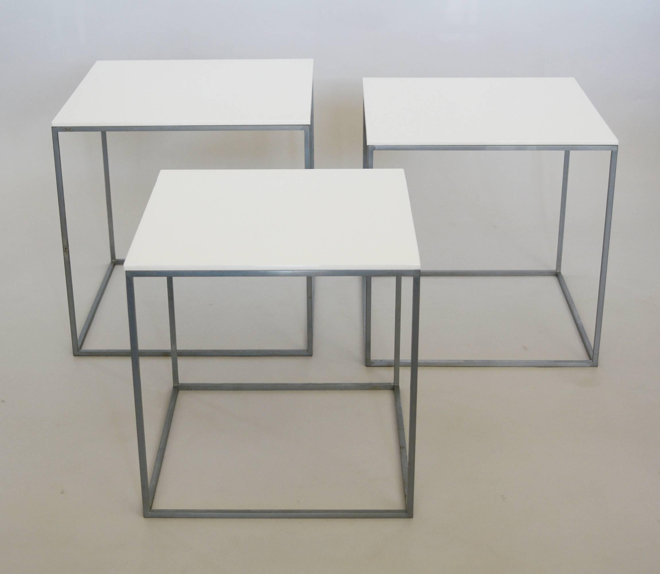 Three small nesting tables by Poul Kjaerholm. They have a matte chrome-plated finish on steel with white acrylic tops. The smallest table is stamped 