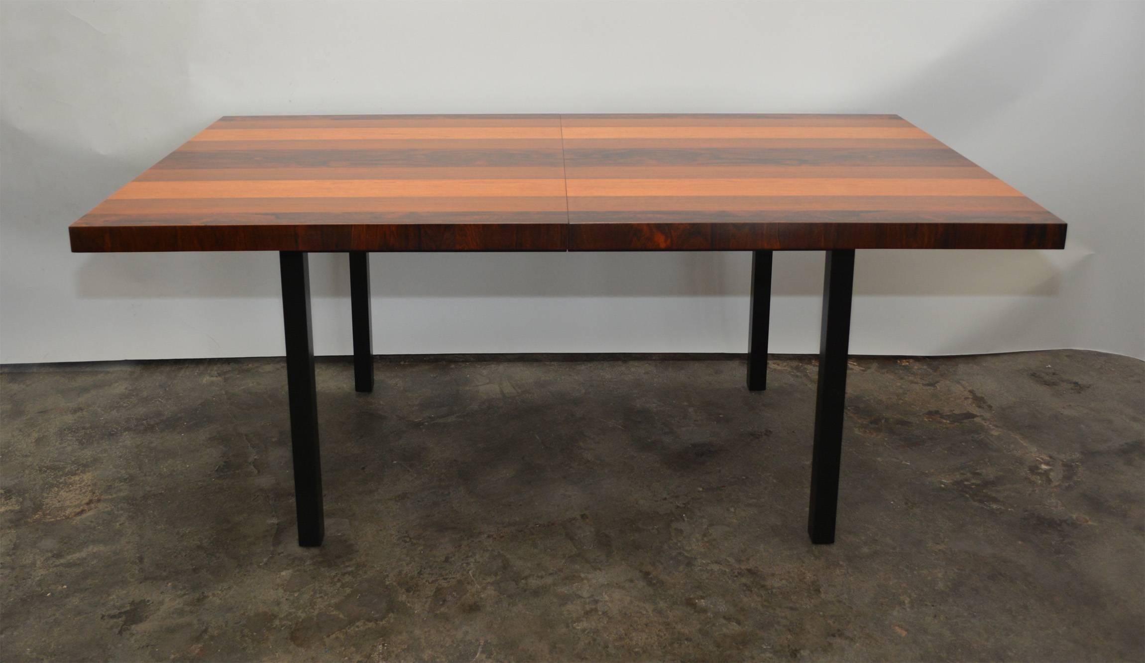 This large dining table has a banded top of rosewood, walnut and ash. The edges of the table are in rosewood. The base is a satin black. The table has been refinished. There are two 20