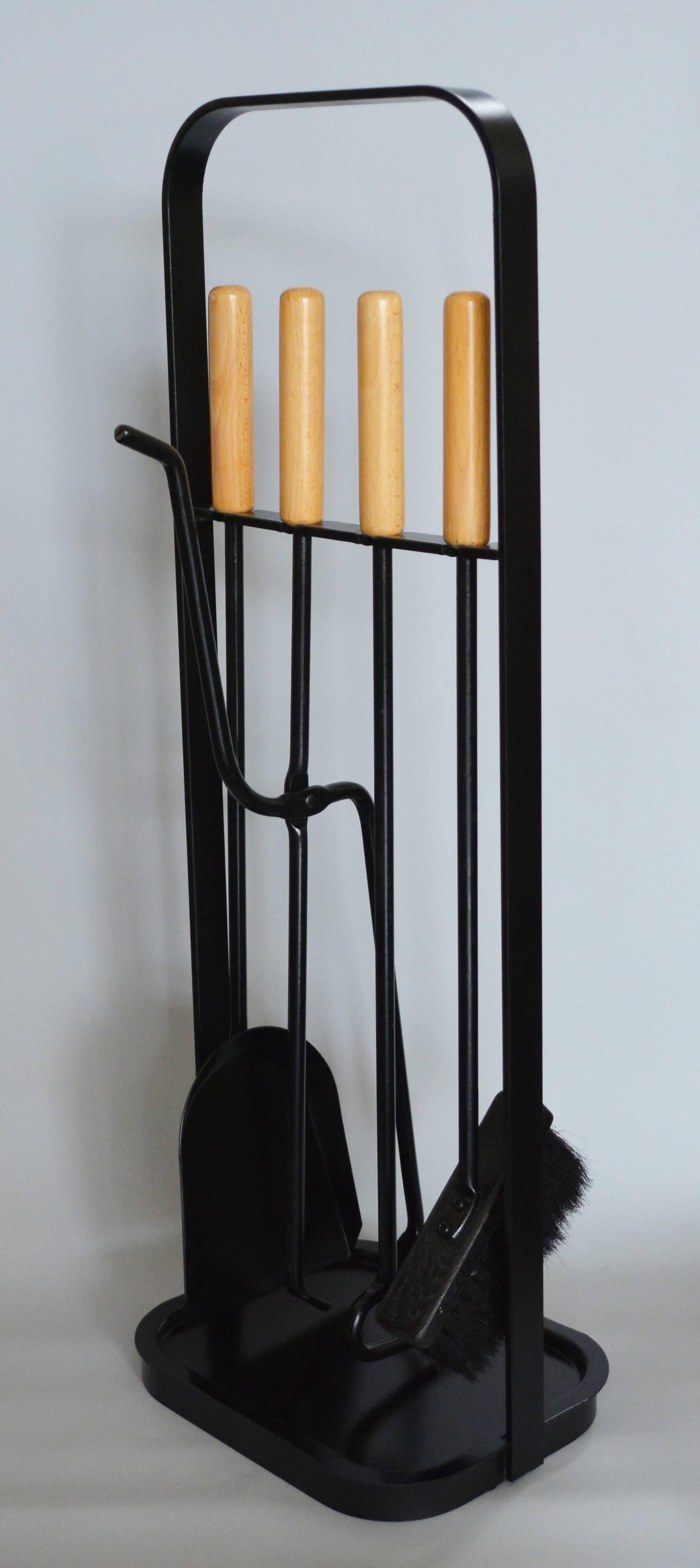 Set of modernist iron fireplace tools. These have beech handles. This simple clean lined set has a sculptural quality to it. The set includes a poker, broom, dustpan and log grabber. The tray at the bottom is removable.