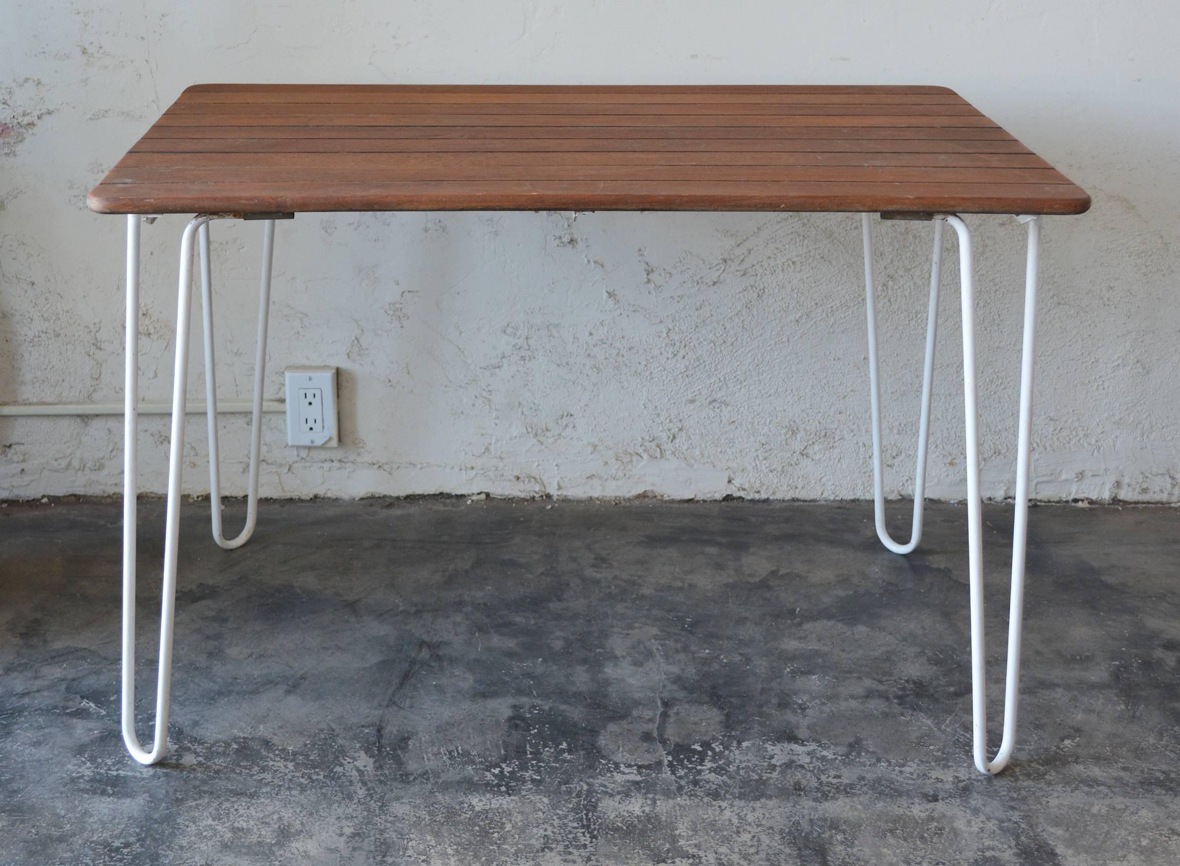 Small teak and iron dining table. This table has legs that are easily removed by sliding the end out of a bracket underneath the top. The top is made of solid teak boards. The metal has an older repaint. This table is a little lower than a normal