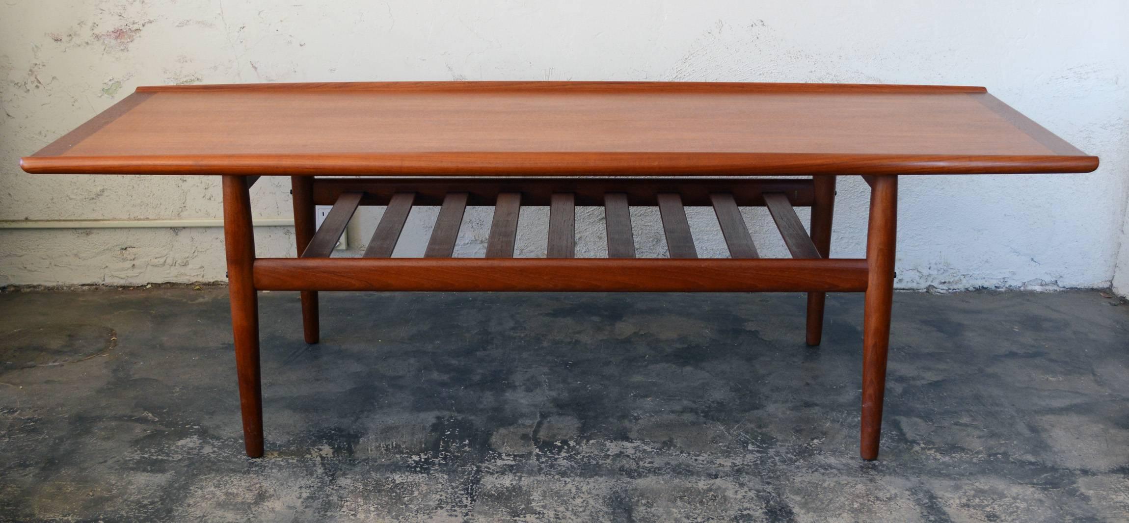 Long Mid-Century teak coffee table designed by Grete Jalk for Glostrup. This has a slatted shelf below the top perfect for magazines or books. This table has it's original finish that shows minimal wear.