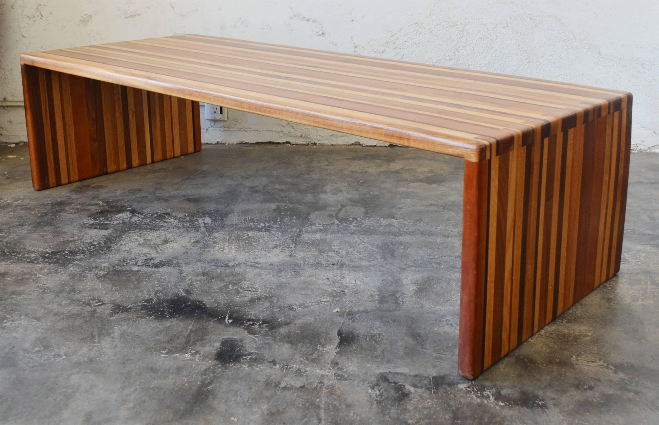 Table ou banc en bois mixte stratifié fabriqué en Studio. Cette table est composée d'au moins cinq variétés différentes de bois dur. Les extrémités sont reliées par des queues d'aronde. Il y a une rayure plus profonde sur un côté, le long de la