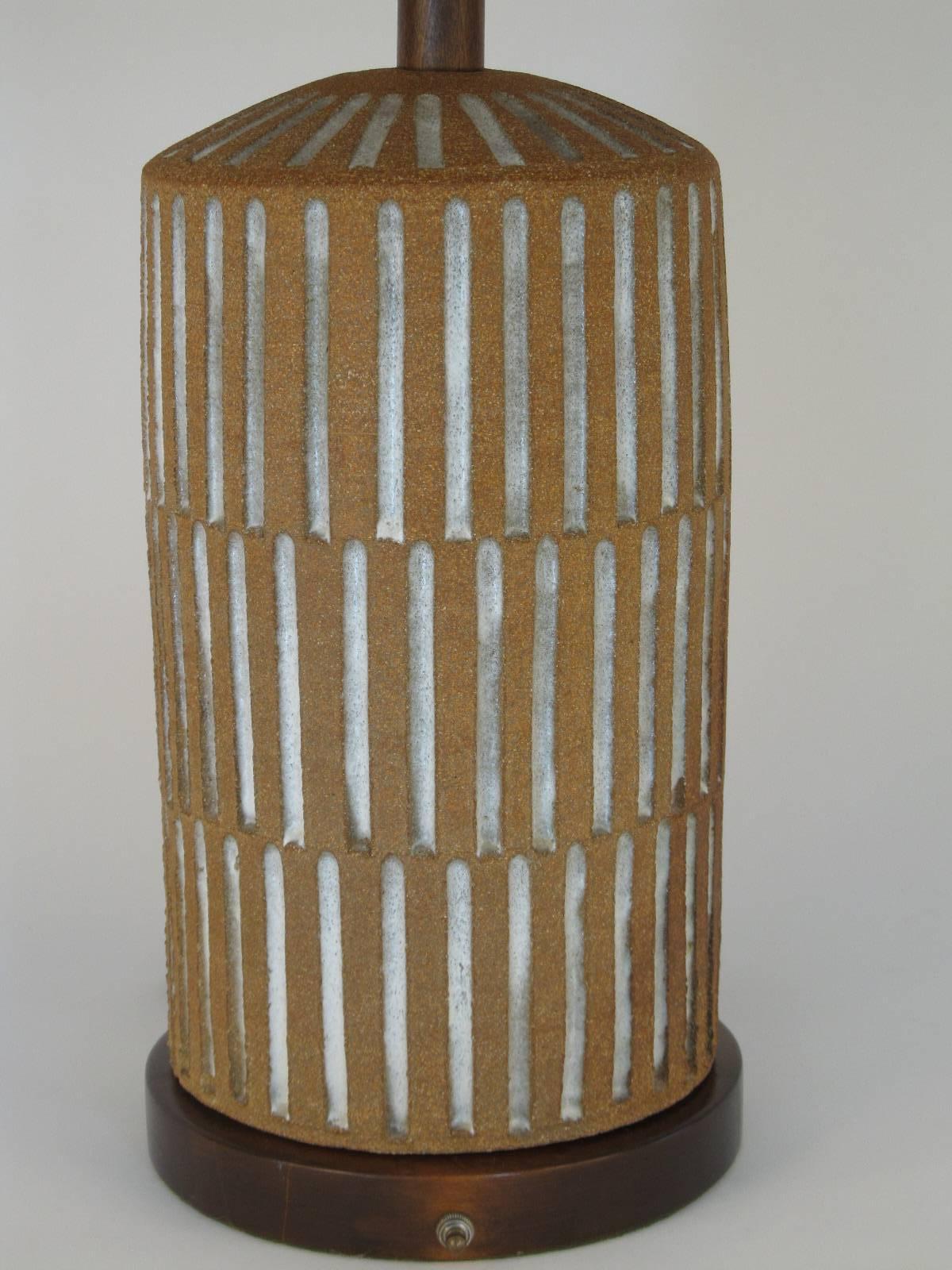 An artfully handmade ceramic lamp with a colonnade or coliseum style of sculpted relief. The body of the piece is glazed and unglazed ceramic. The base and top stem are walnut.