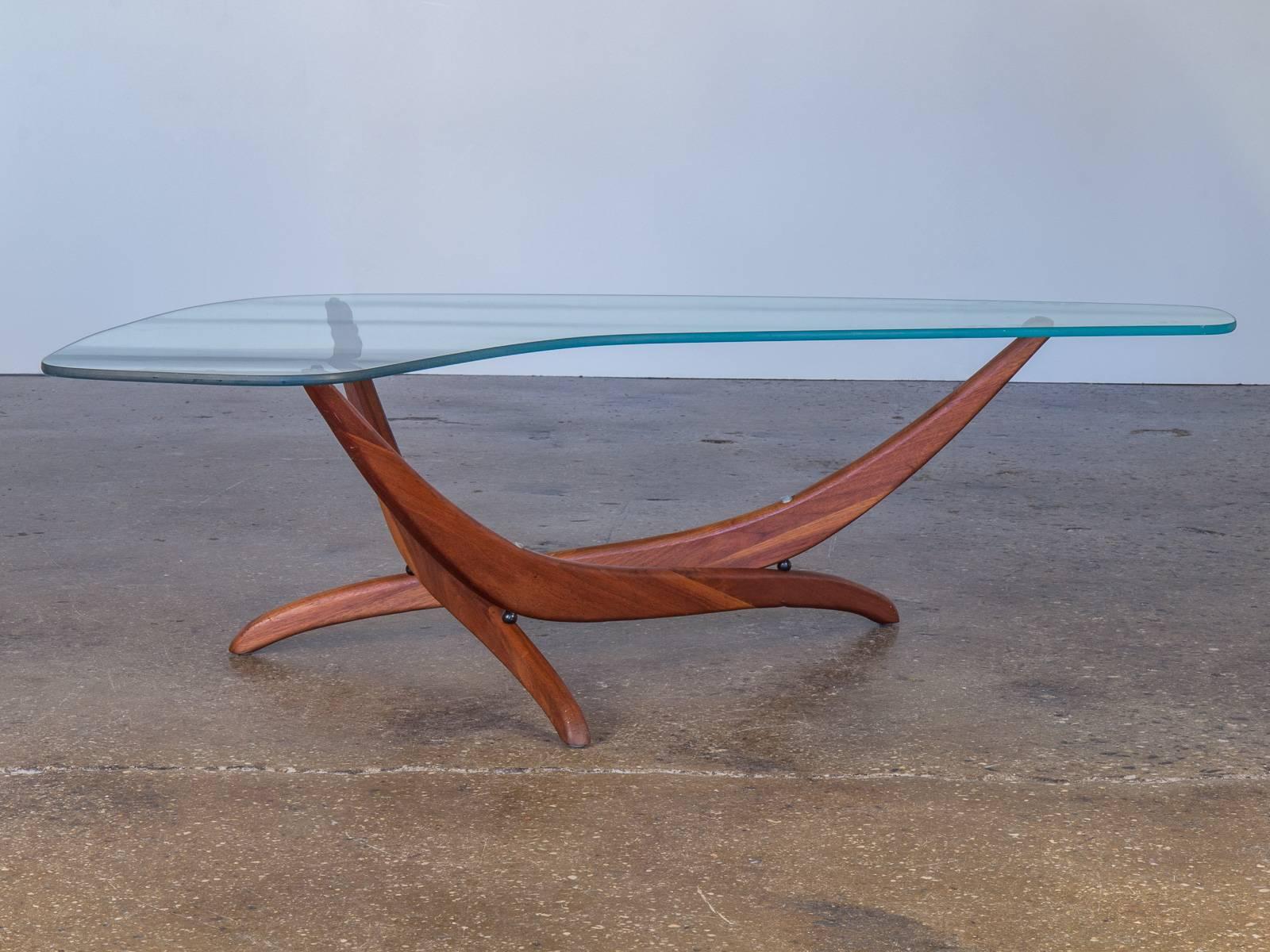 A boomerang glass top in pristine condition sits on a sculptural walnut base in this 1960s Forest Wilson table. Thick, green-edged glass. The base presents an enticing new shape from every angle. In excellent condition.

See our matching Wilson