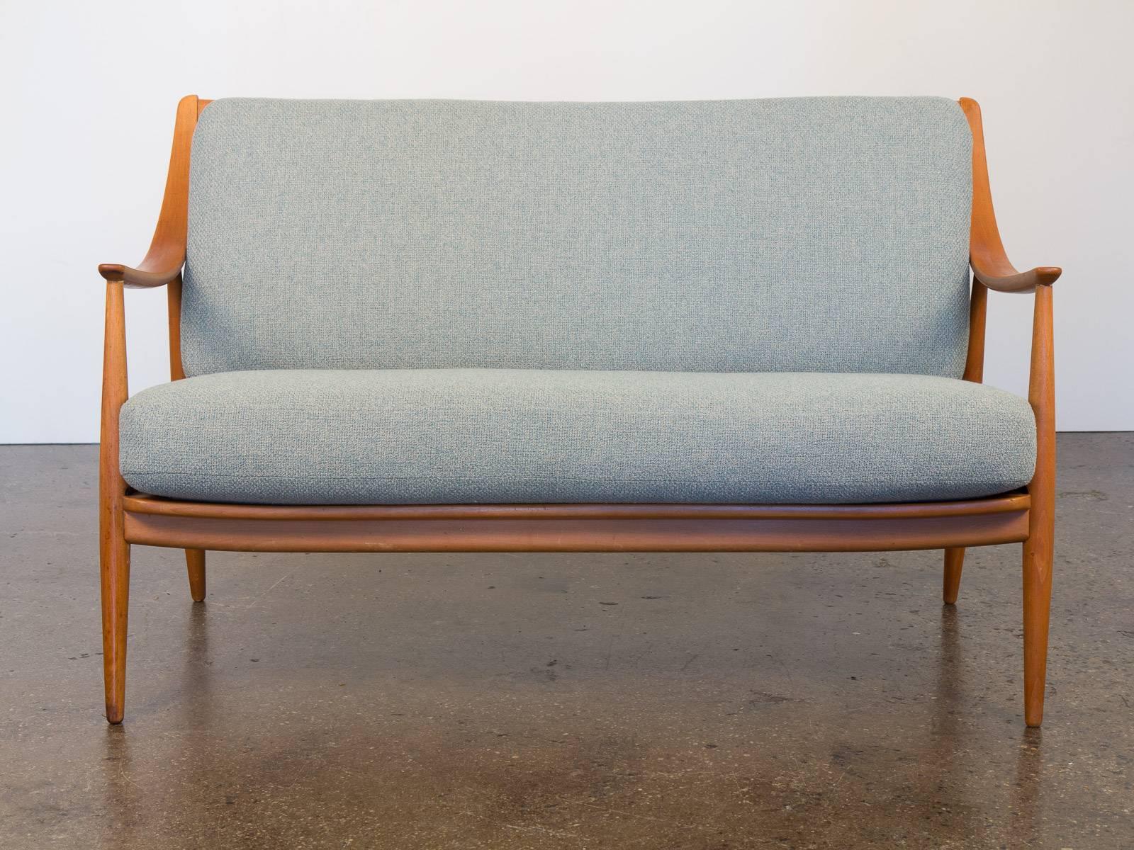 A graceful loveseat designed by Peter Hvidt and Orla Mølgaard Nielsen for France and Son. This sofa boasts sculpturally swooping armrests in a birch patina with a view that continues to the spindle backing. Newly upholstered in a soft robin's egg