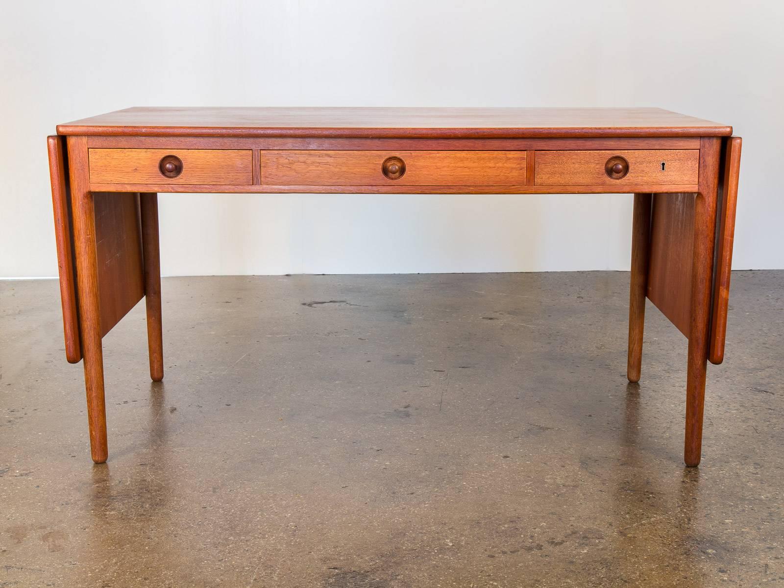 Scarce Danish oak and teak AT305 pencil desk by Hans Wegner for Andreas Tuck. Desk has a lovely age-appropriate patina with three long pull-out drawers. With the option of having the drop leaf open on one side, closed, or fully extended, it is a