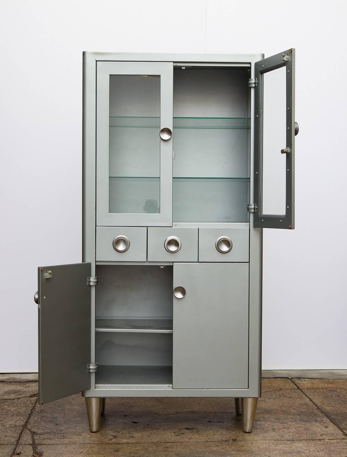 1950s Modern Industrial display cabinet manufactured by American Metal Furniture, Inc. This heft yet sleek Norman Bel Geddes inspired steel cabinet has round disc pulls on the drawers and cabinet doors. Upper display doors are equipped with two