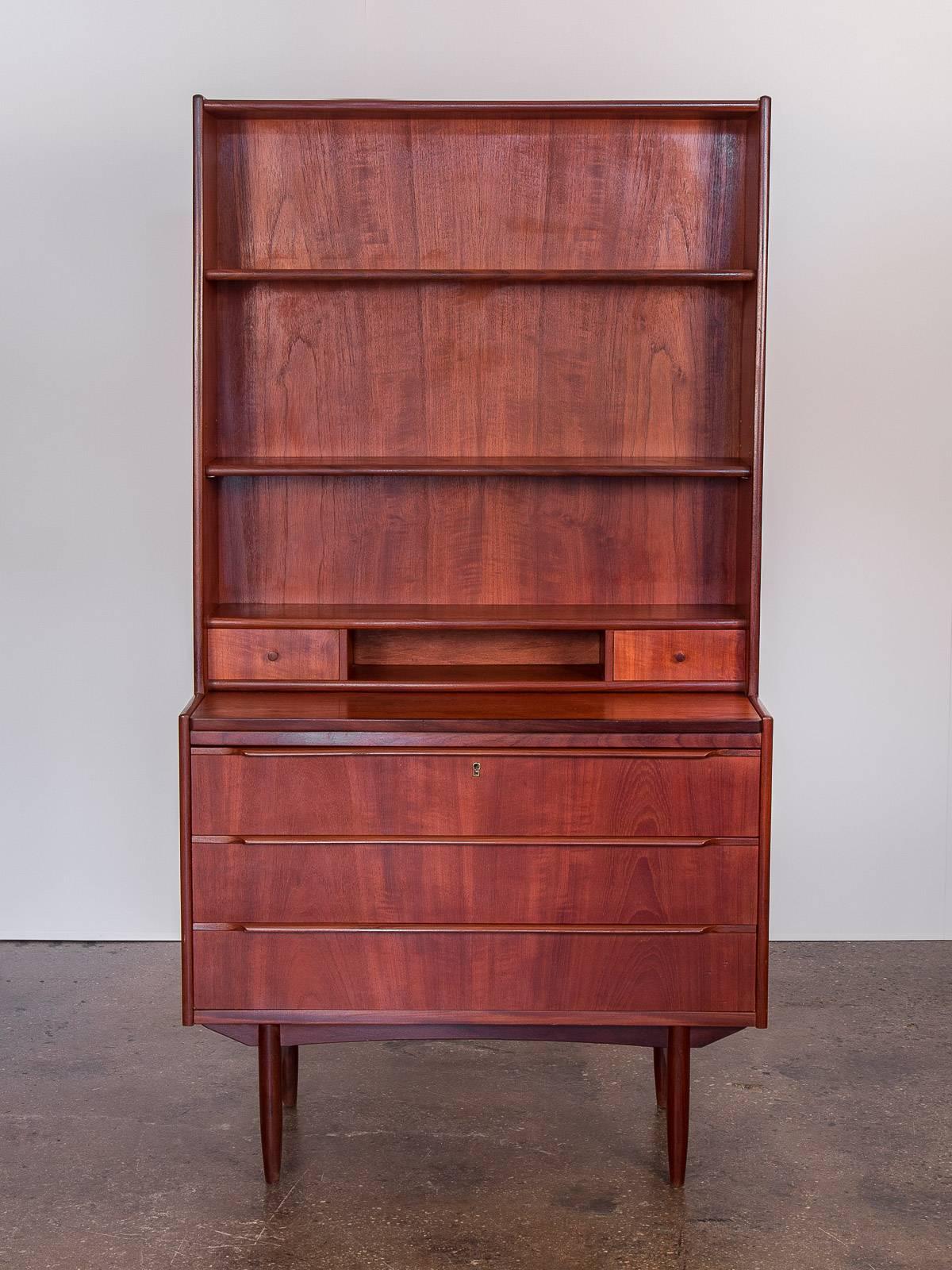 This attractive, gleaming Danish modern teak secretary dates to the 1960s. The top shelves are adjustable for two alternative heights and measure 7.5 inches deep. Two small desk drawers and three large drawers on the bottom provide versatile