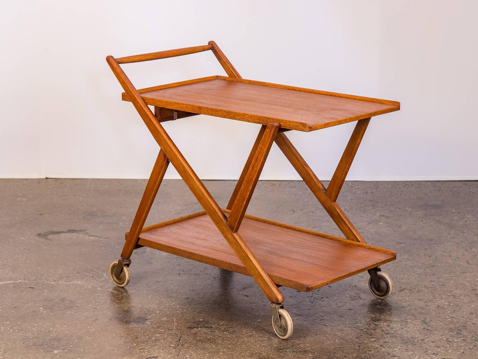 1960s Danish modern teak bar cart trolley in good vintage condition. This newly polished cart features two-tier trays for small plates or beverages. Great for entertaining or as a stationary side-table. When not in use, the collapsible ability makes