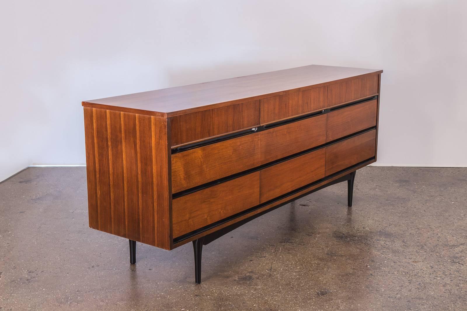 Mid-Century Modern triple dresser. This 1960s, sturdy walnut dresser has nine drawers for ample storage, and features ebonized drawer handles and legs. The walnut wood selection has a lovely, distinct grain to admire. Slight discoloration spot on