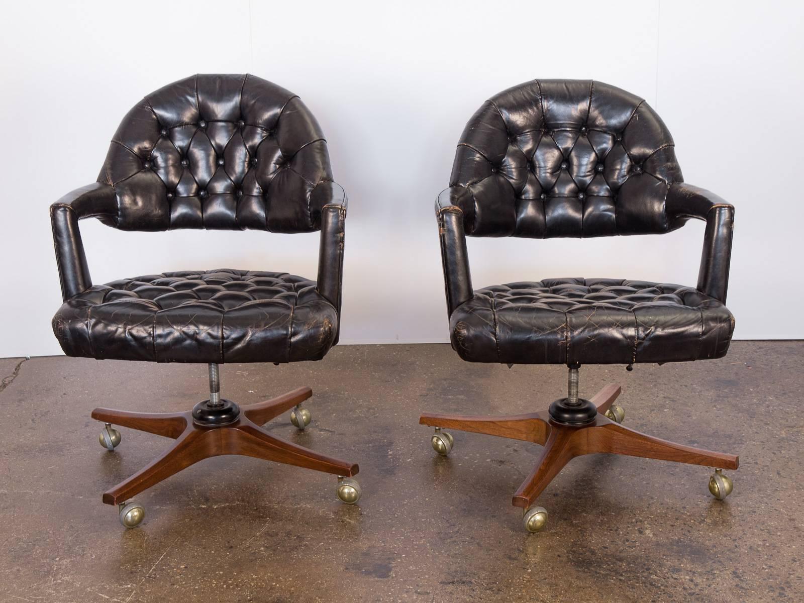 1950s open-back, tufted leather swivel chairs by Edward Wormley for Dunbar. These stylishly worn desk chairs feature an open-back form with angular, padded armrests. The tufted black leather is supple and sumptuous with a gorgeous patina. Adjustable