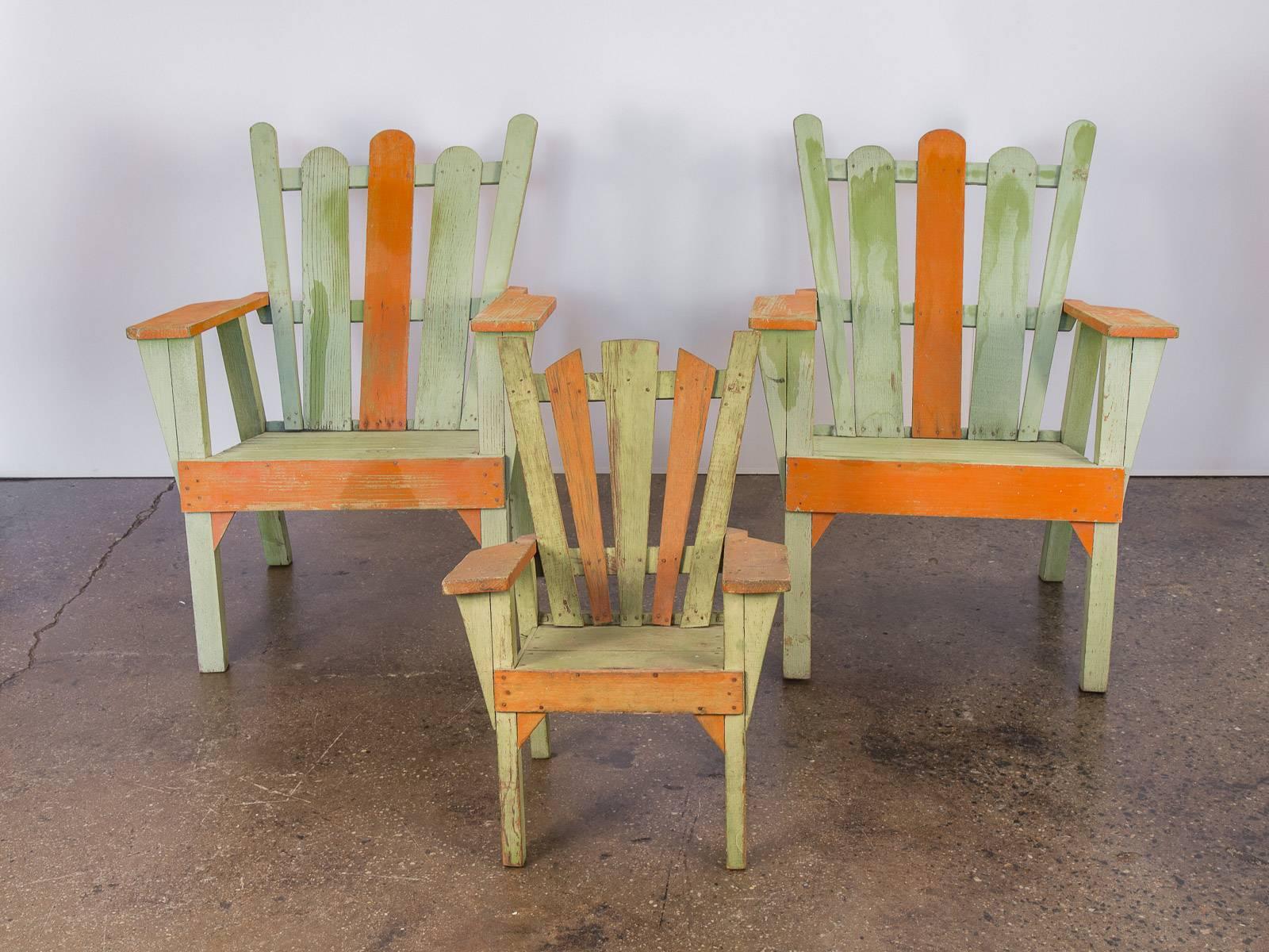 Set of three 1960s vintage Adirondack lounge chairs. Consists of two larger chairs and one adorable child’s sized chair. The paint and wood has age-appropriate wear, but are sturdy without waver. Stained in a colorful light moss-green and orange,