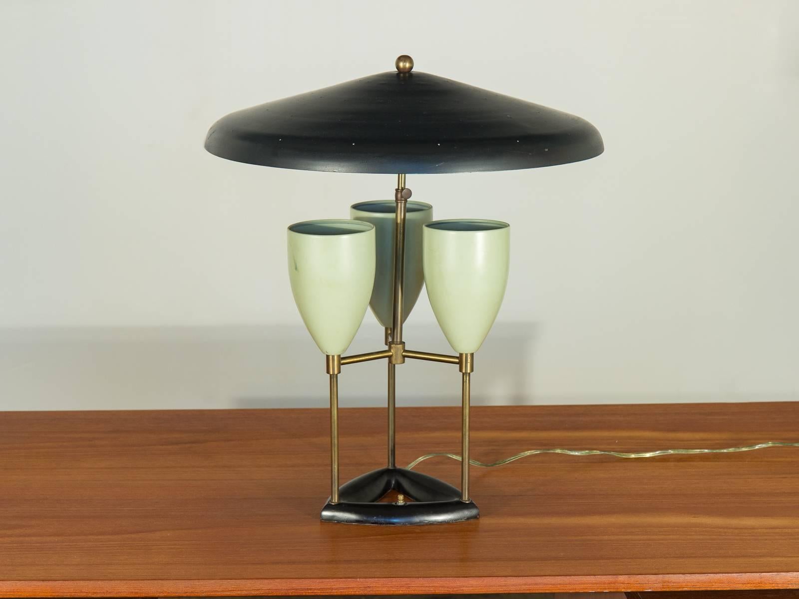 This three-light desk or table lamp in the style of Greta Grossman is attributed to Gerald Thurston for Lightolier. A large pierced metal shade and pale green fixtures are connected by a brass framework. An original and scarce design. The lamp is in