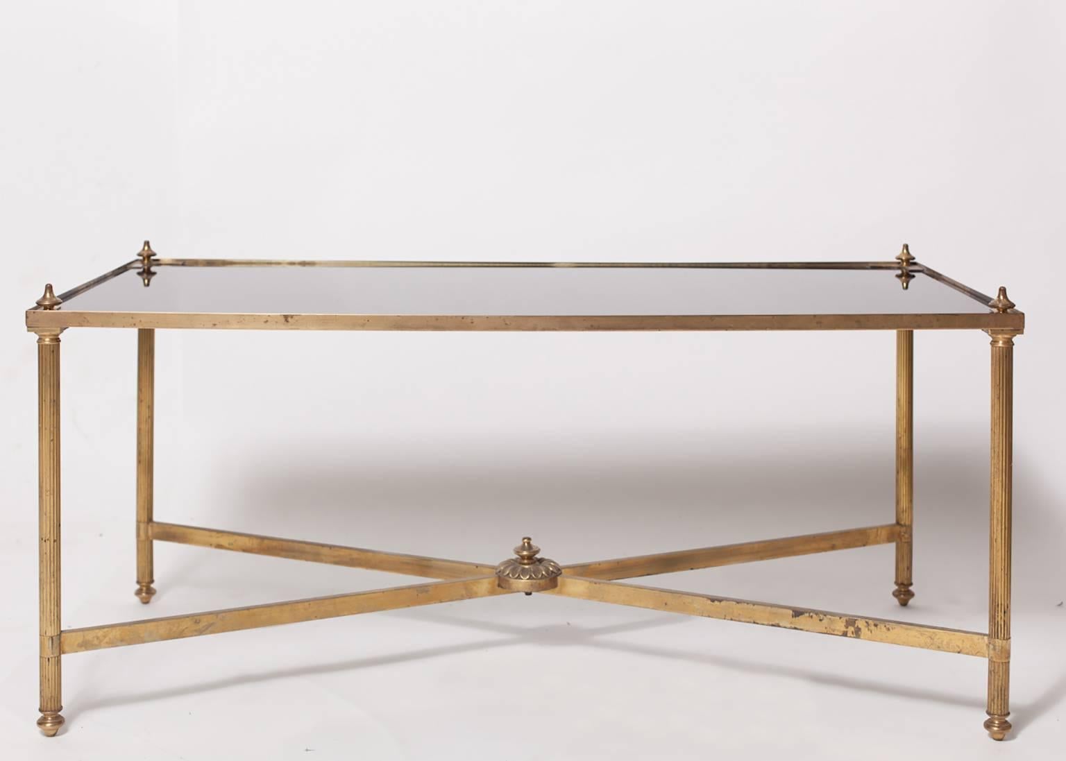 French Maison Jansen neoclassical style brass coffee or cocktail table with black glass top; the rectangular glass top fitted within corner spandrels; raised on reeded supports all joined by an x-form stretcher.