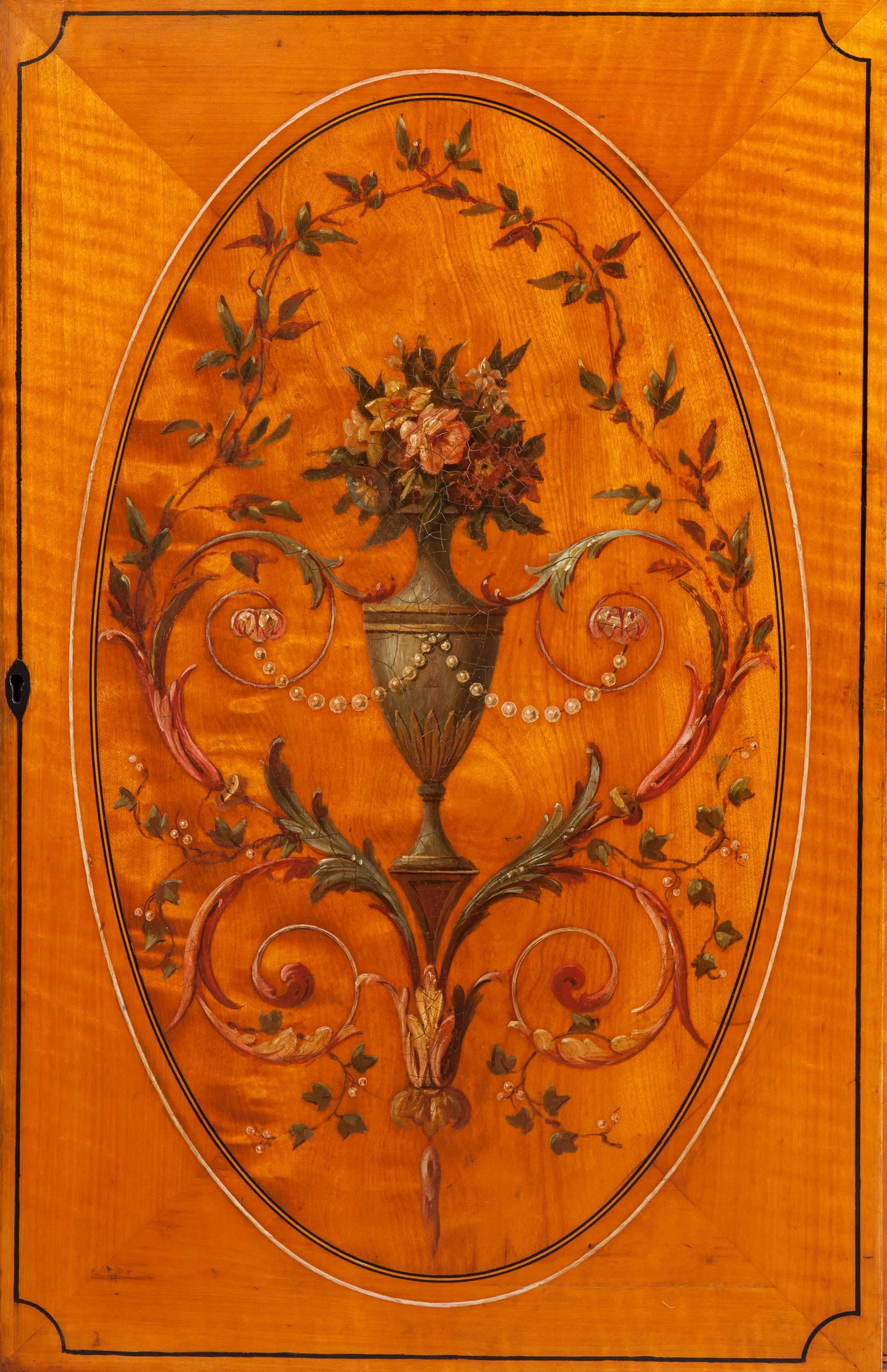 A library bookcase in the manner of Sheraton and the Adam Brothers.

Constructed in satinwood, line inlaid, and hand decorated in polychrome; of breakfront form, rising from swept bracket feet, the lower part having four lockable cupboards,